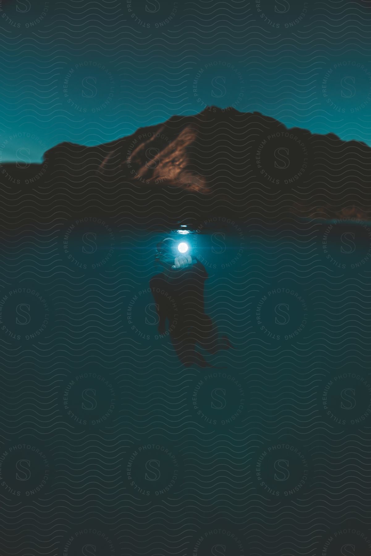 A man scuba diving underwater near a mountain region on the coast at night