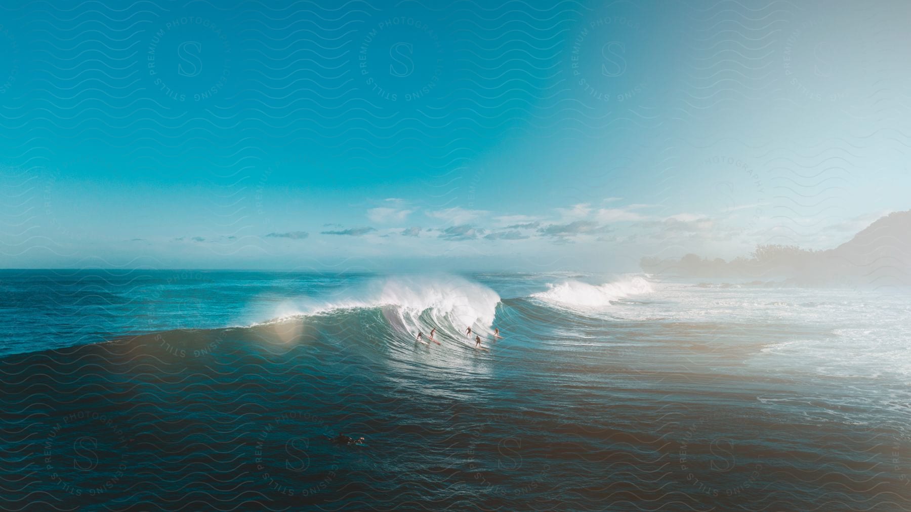 Waves breaking close to the coast next to a mountain range under a blue sky