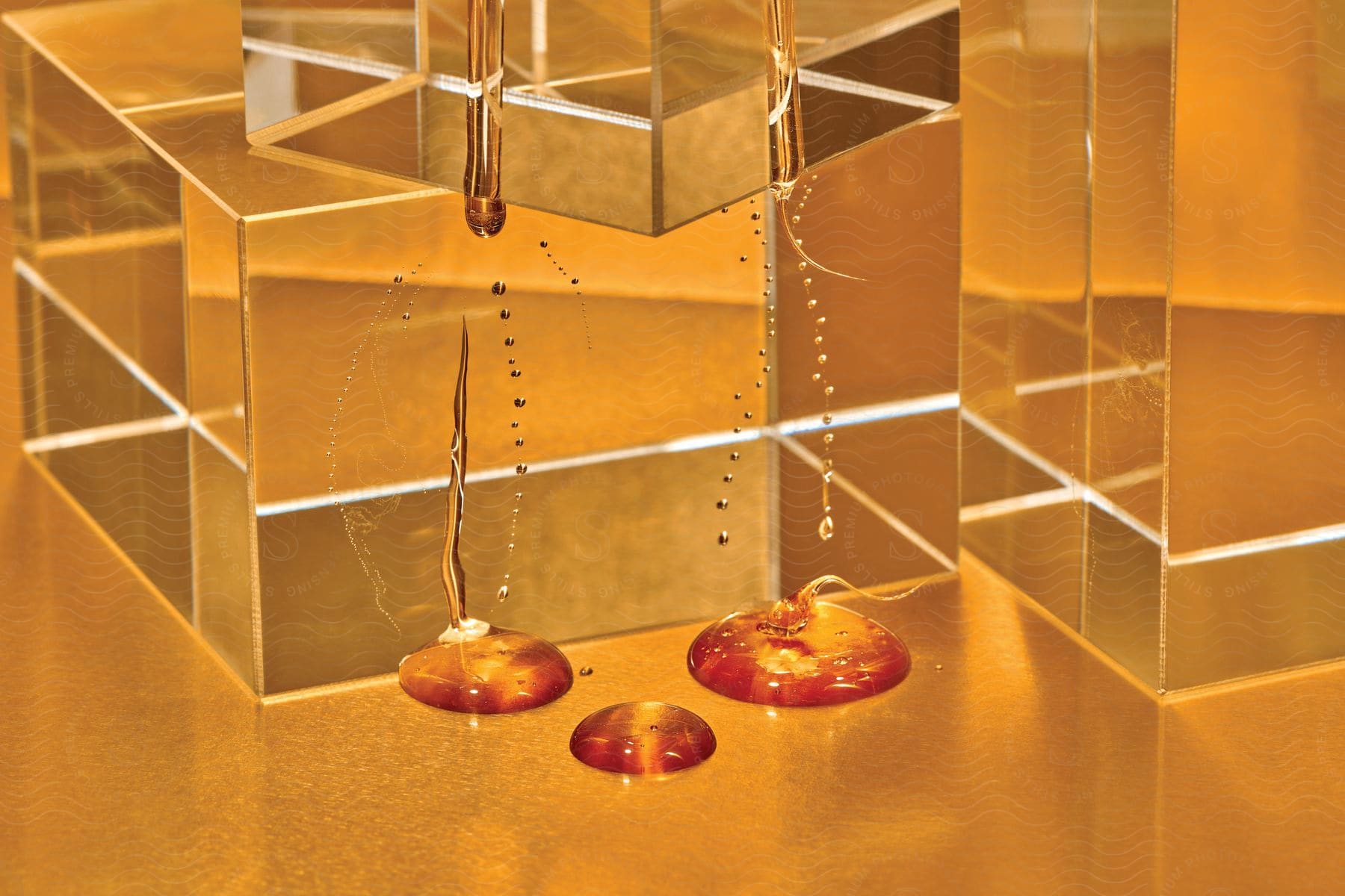 Glass boxes on a glass table under an orange light with liquid falling from them in three domes on the table clear cubes abstract