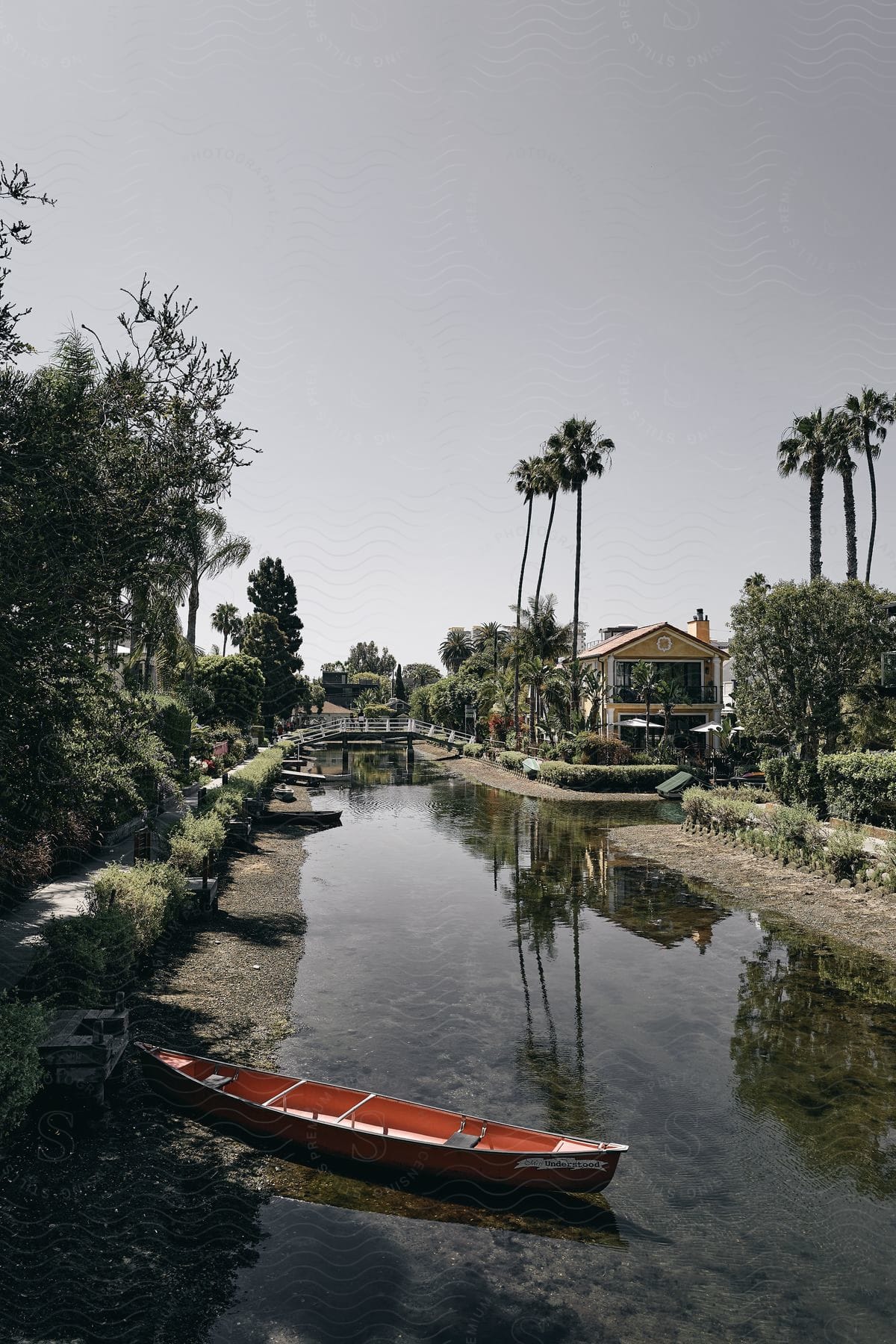 A small red canoe is positioned at the edge of a narrow river stream