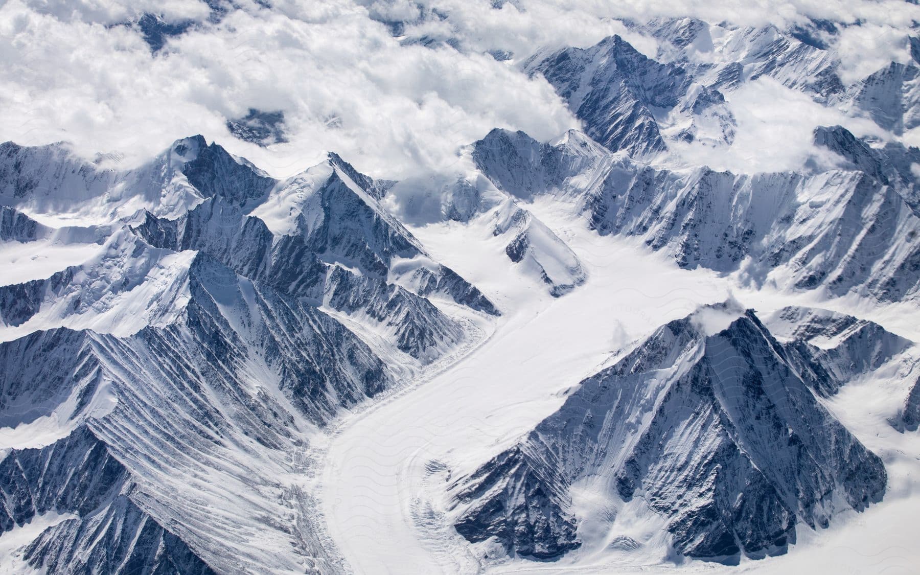 Cumulus clouds match color of the snow covering jagged mountains