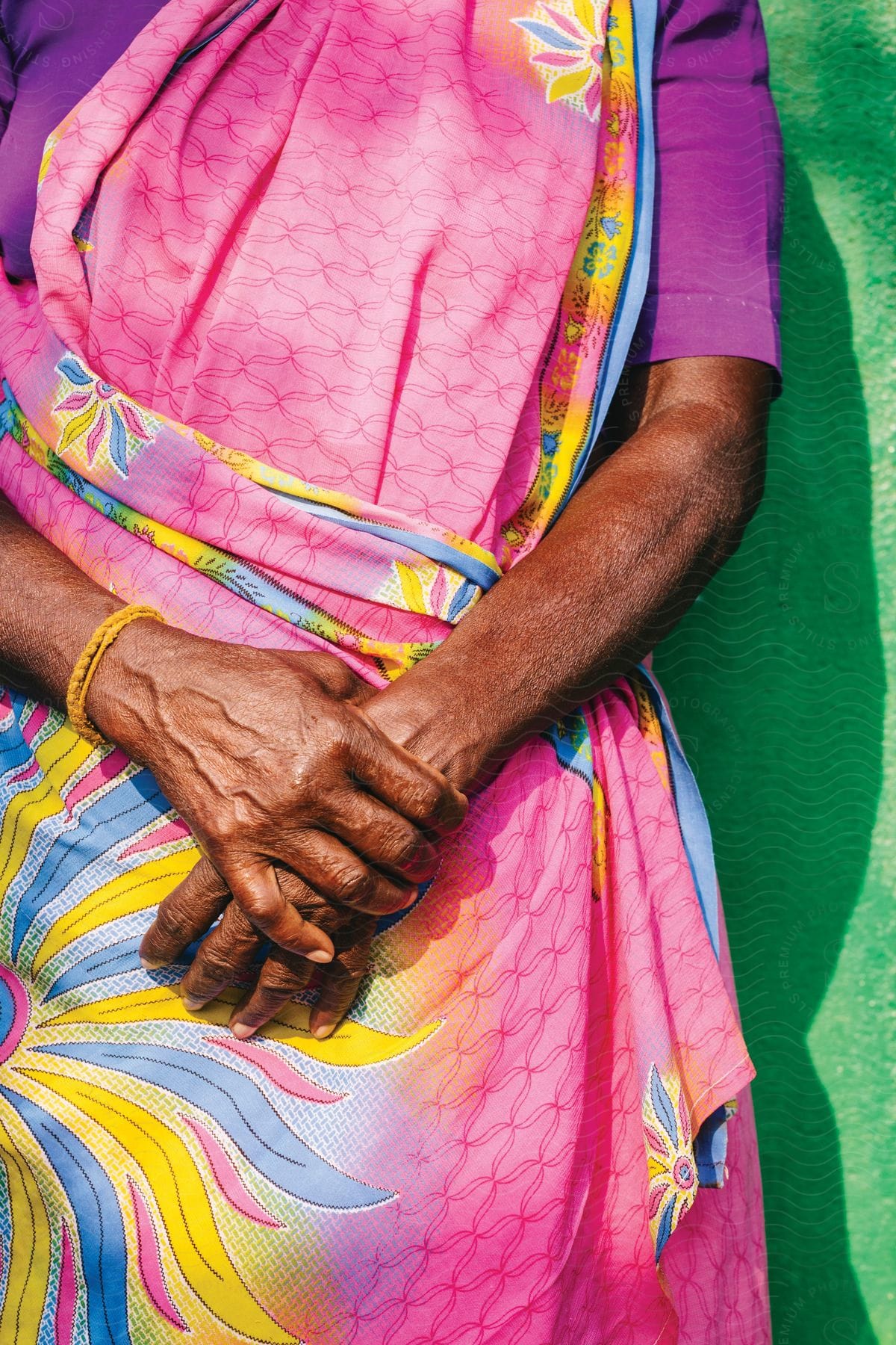 A woman stands with her hands clasped while wearing a pink dress