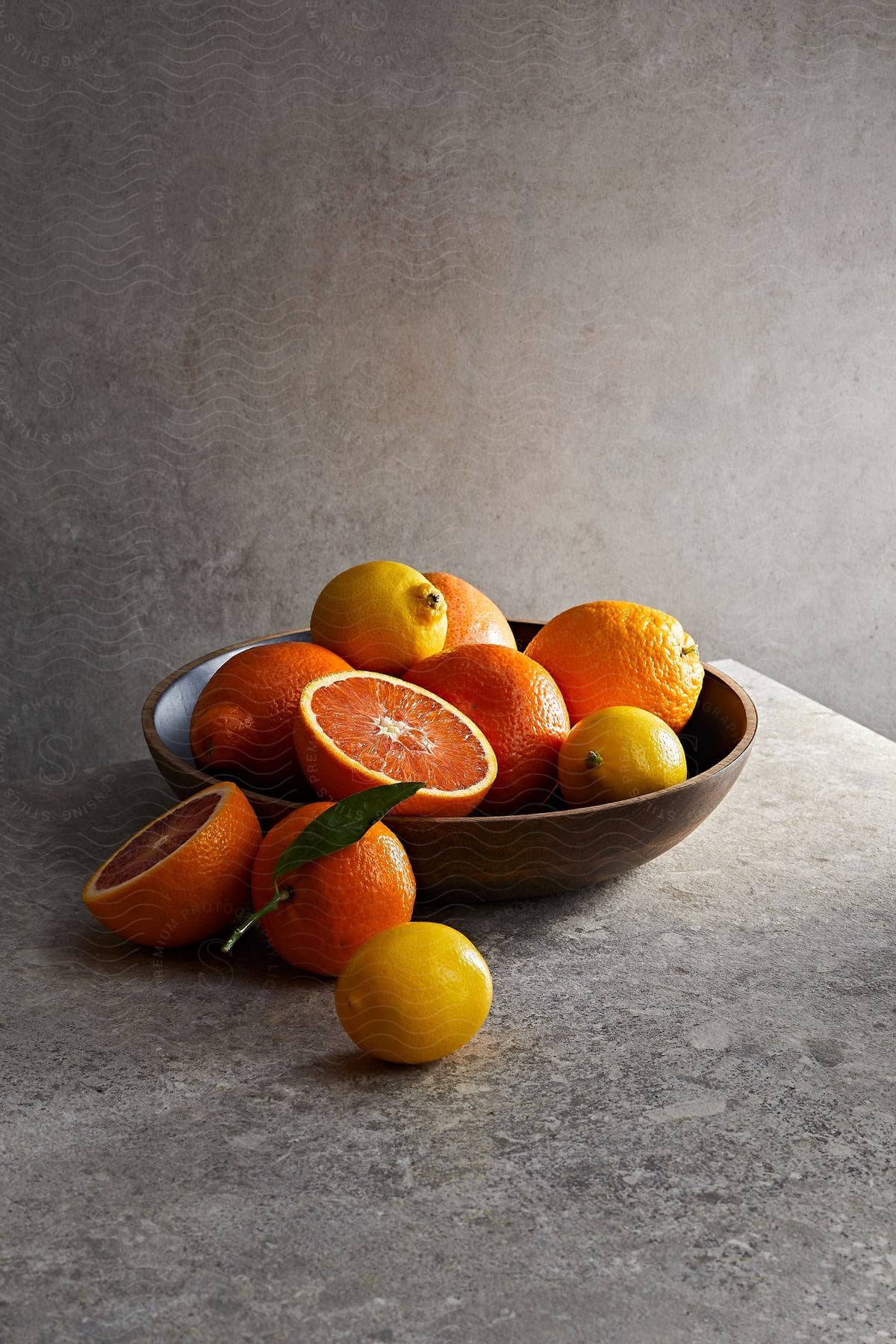 A bowl of citrus fruit with three fallen off to the side