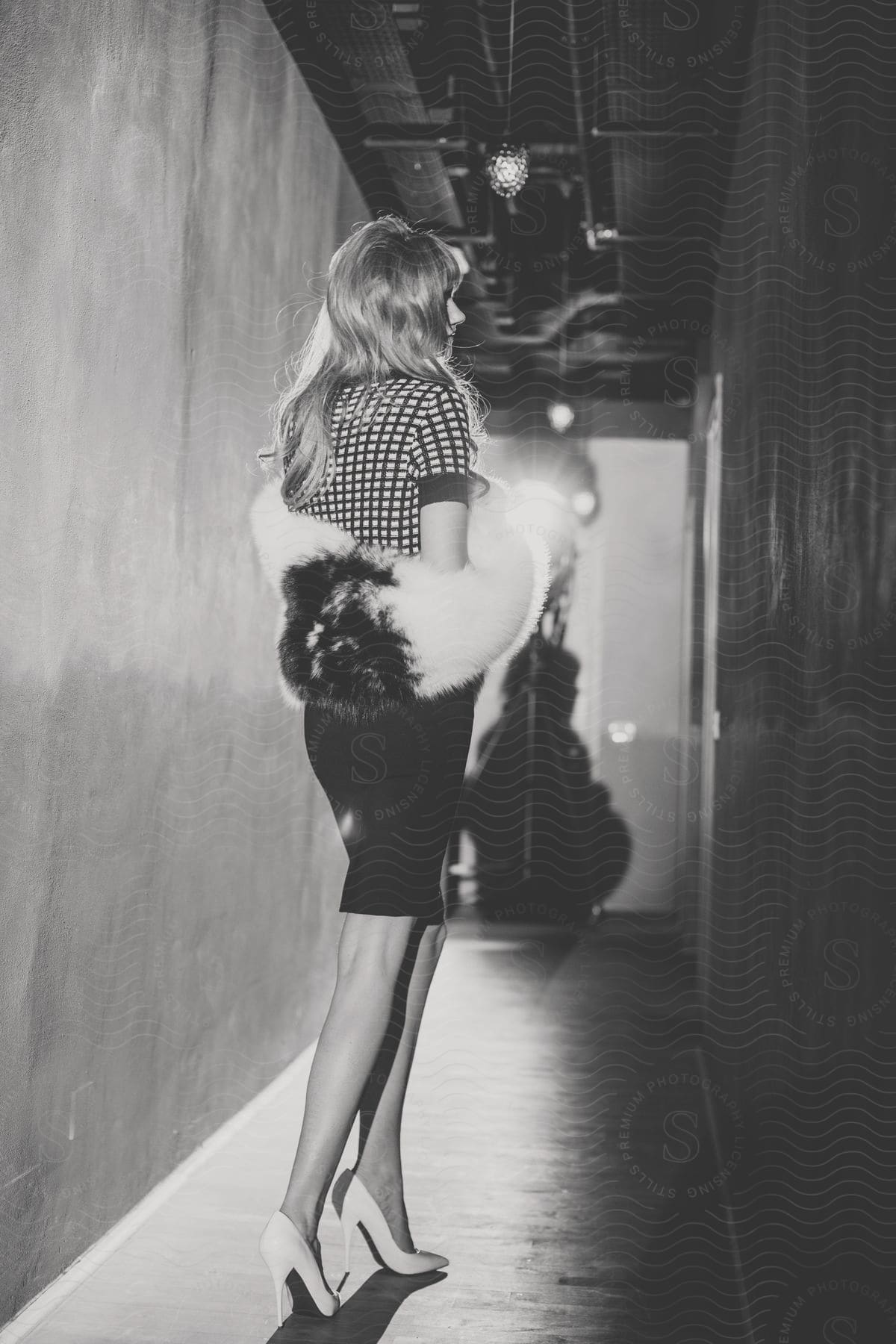 Blonde woman wearing white heels a polka dot blouse black skirt and a twotone fur coat standing in a hall