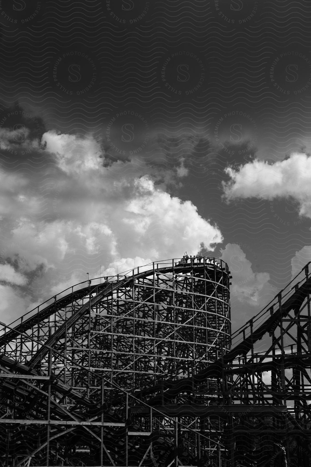 A black and white shot of a roller coaster with people riding under a cloudy sky