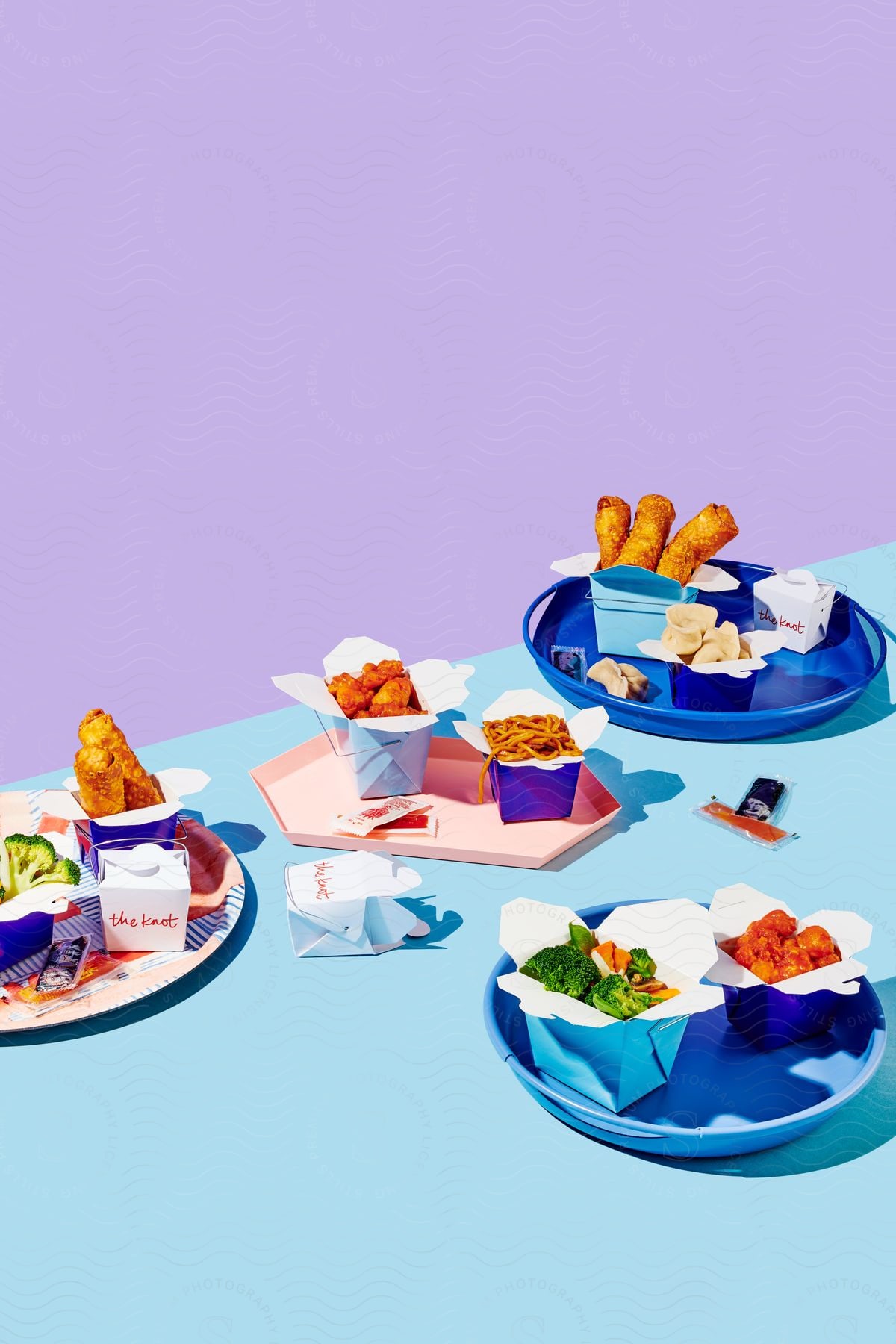 Four trays on a blue table in a purple room each with a different fast food order of chicken fries vegetables and milk