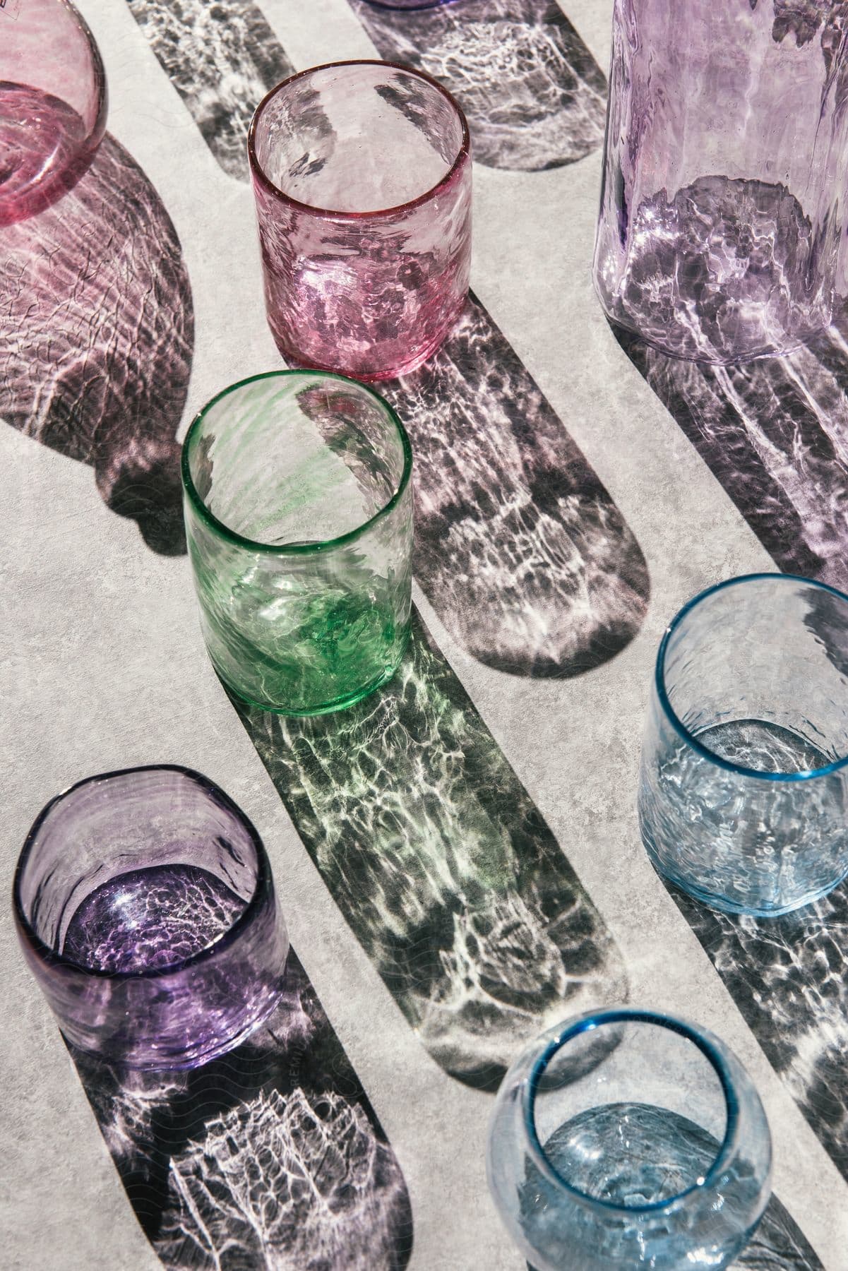 Different colored glasses on asphalt cast colorful shadows of their designs on the ground on a sunny day