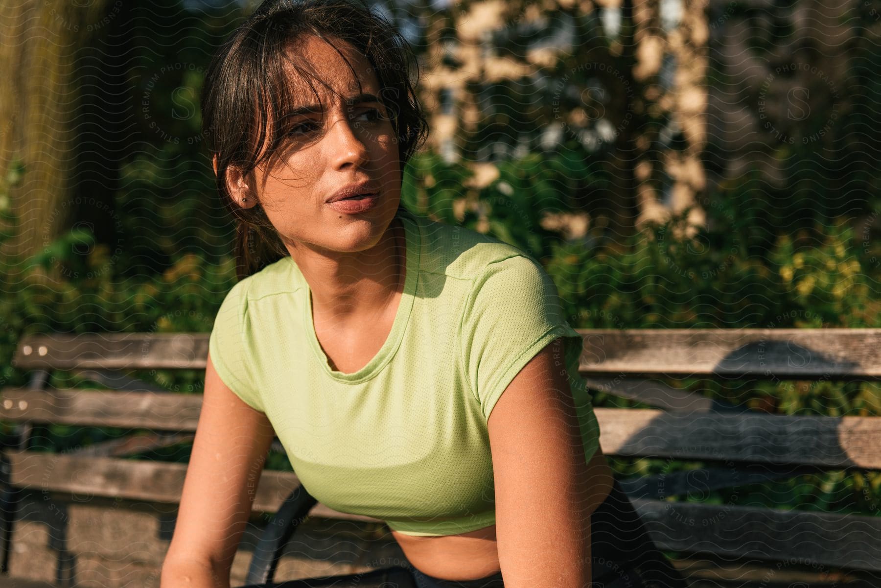 A woman in a green tank top sits on a park bench looking to the side