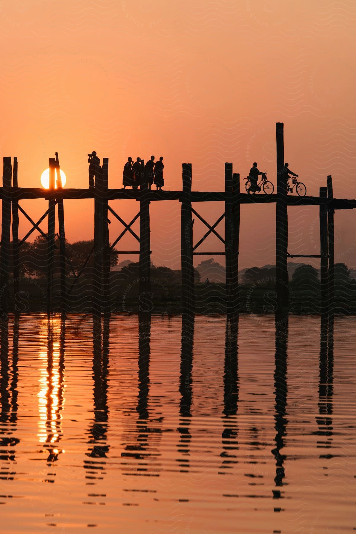 People walking and biking across a narrow pier across the water at sunset