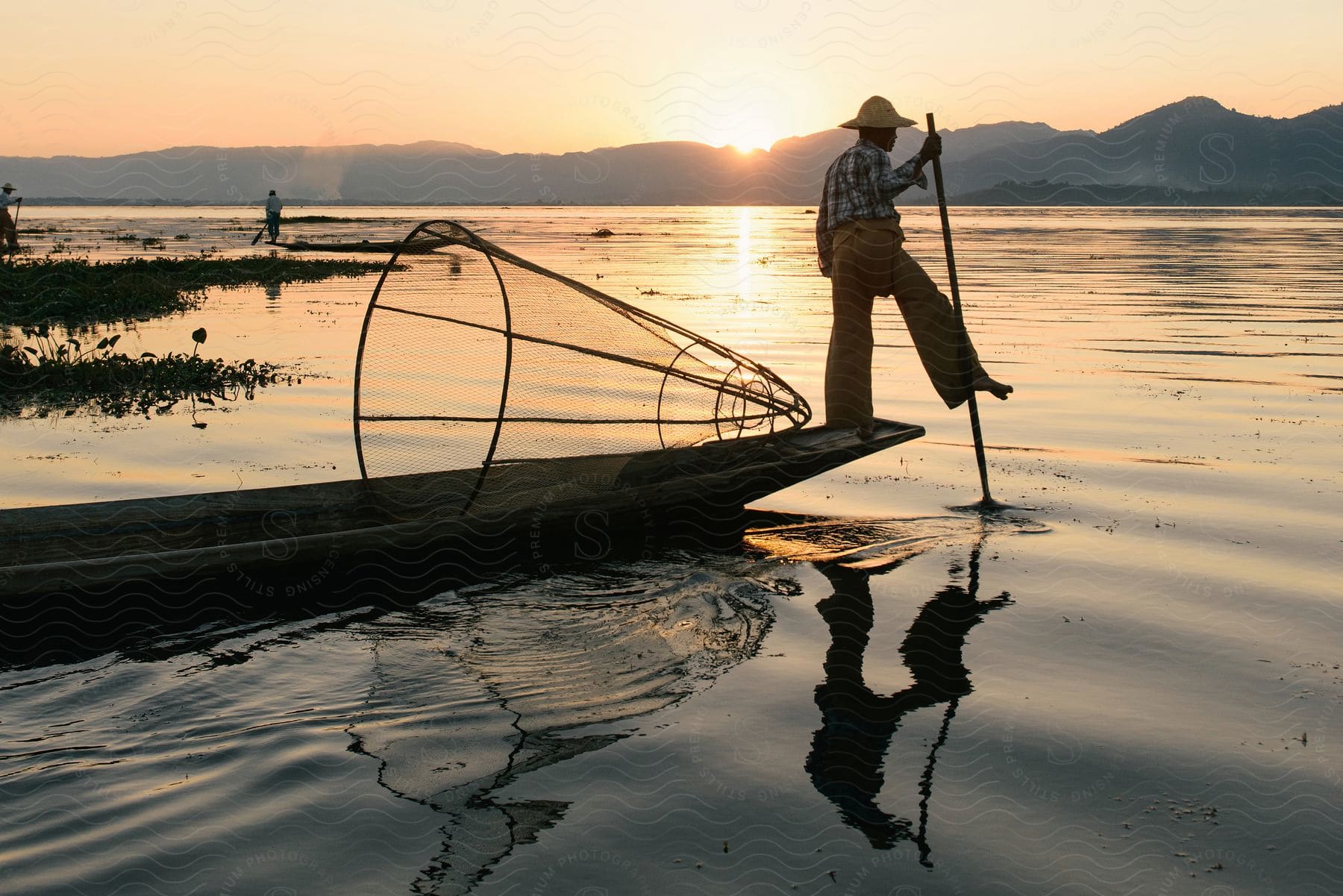 A fisherman drives a canoe with a net in a river surrounded by mountains during sunrise