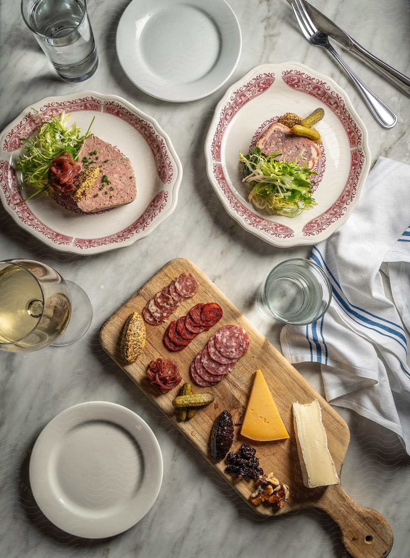 Both wine and water are served with charcuterie and meat dishes on a marble surface