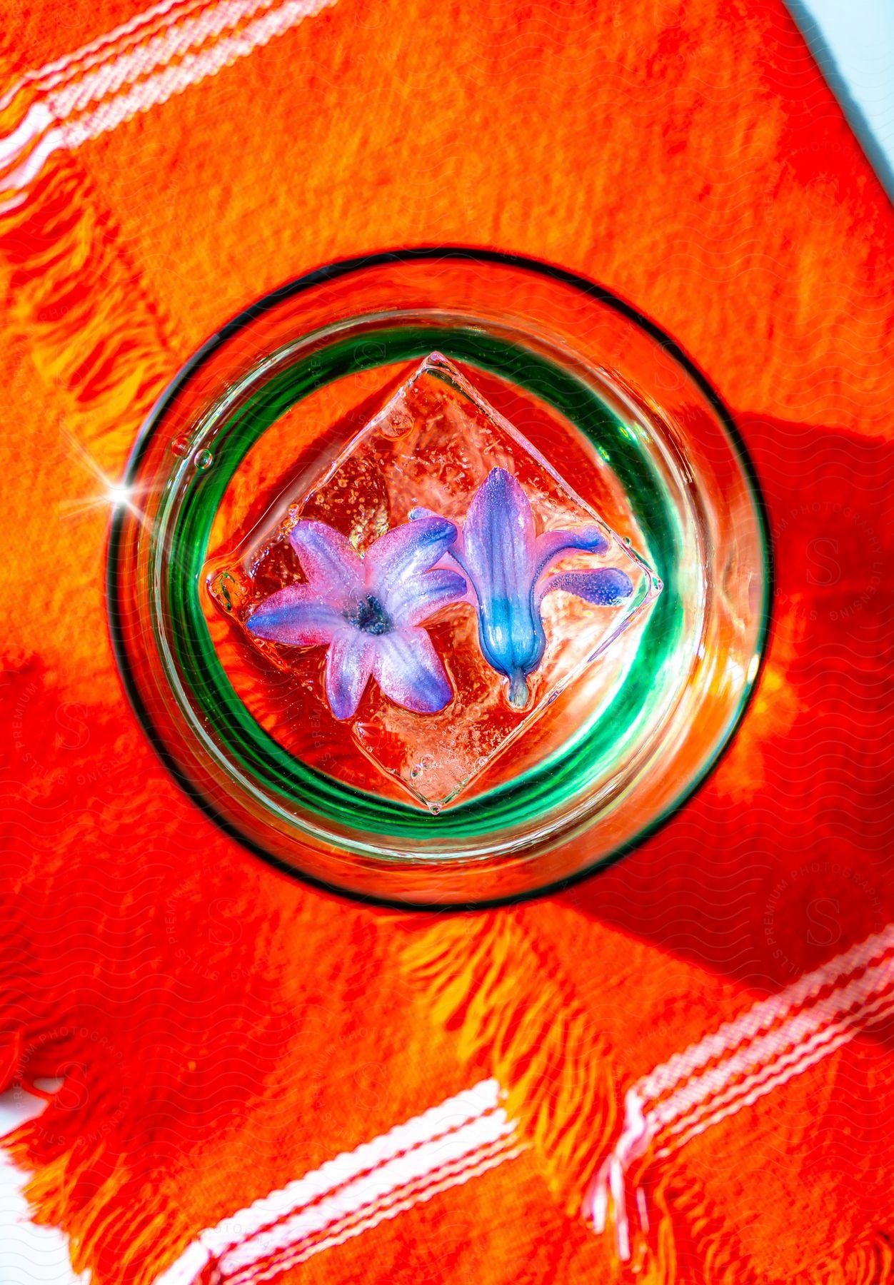 Flowers frozen in an ice cube in an iced drink on an orange cloth