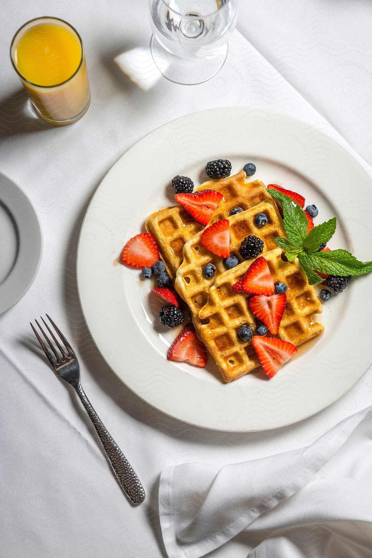 Plate with waffles on a table accompanied by a glass of water and juice