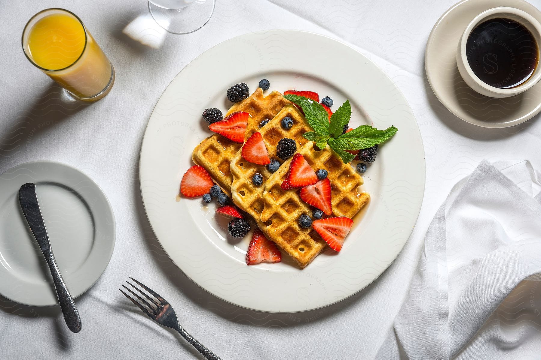 A plate of waffles covered with berries and syrup with a cup of orange juice on the left and a cup of coffee on the right