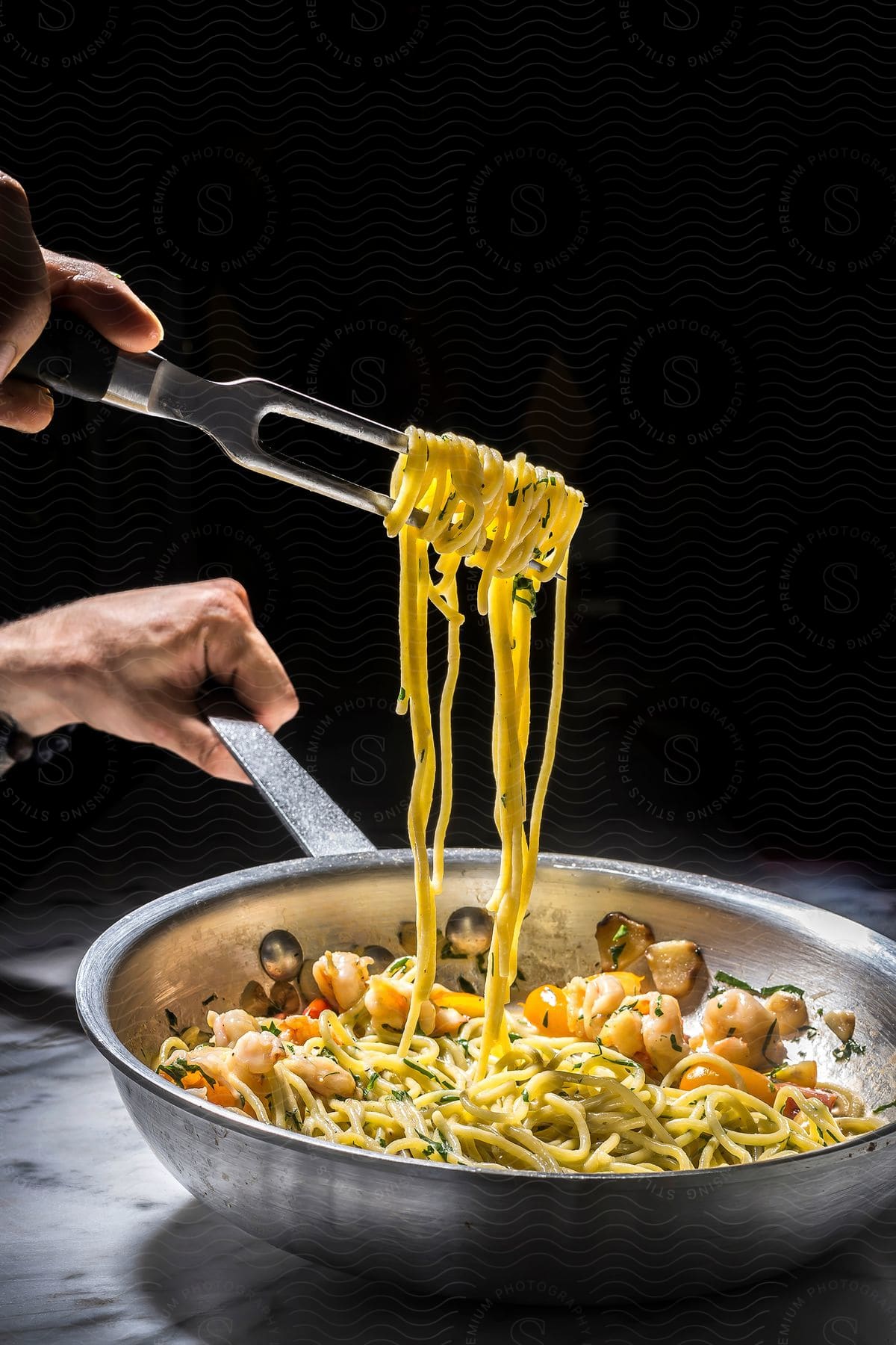 A frying pan cooking seafood pasta with a cooking fork wrapped in it