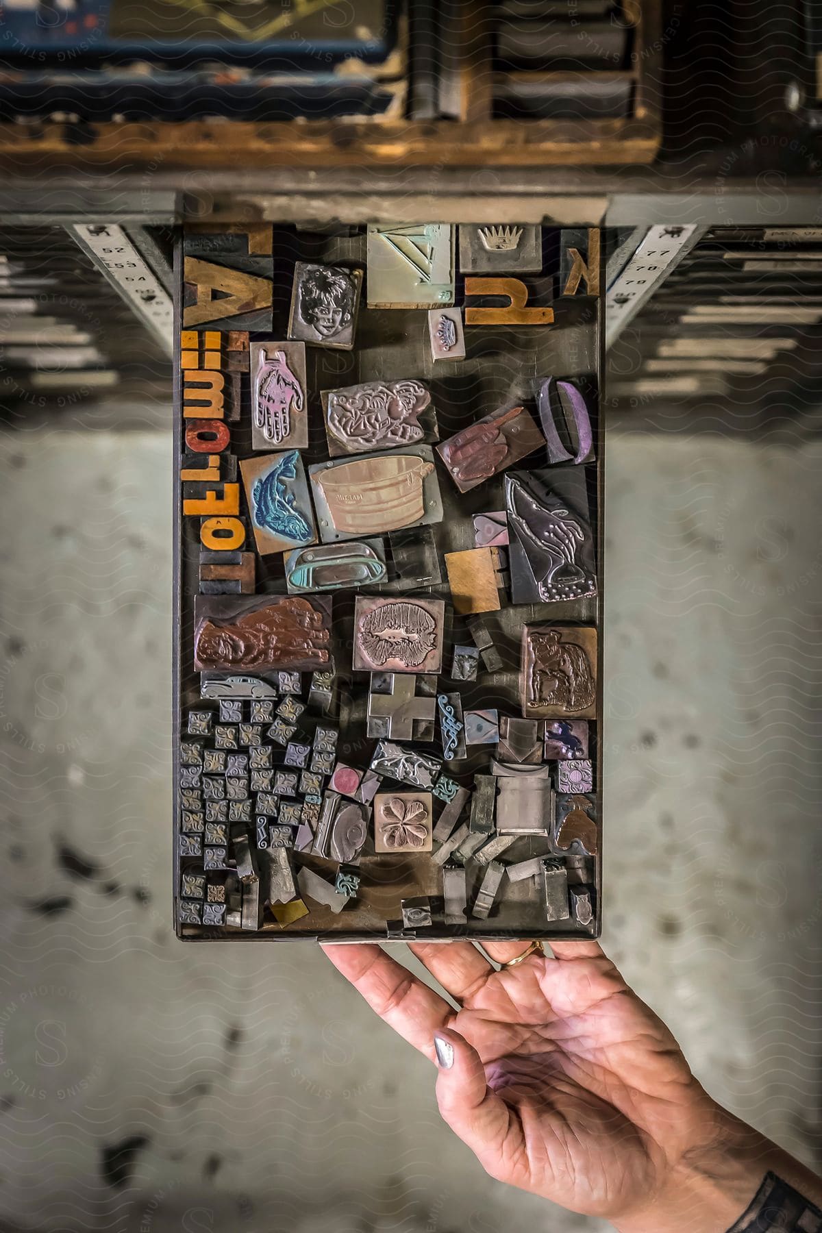 A hand with a tattooed wrist holds out a tray of stamps for a printing press