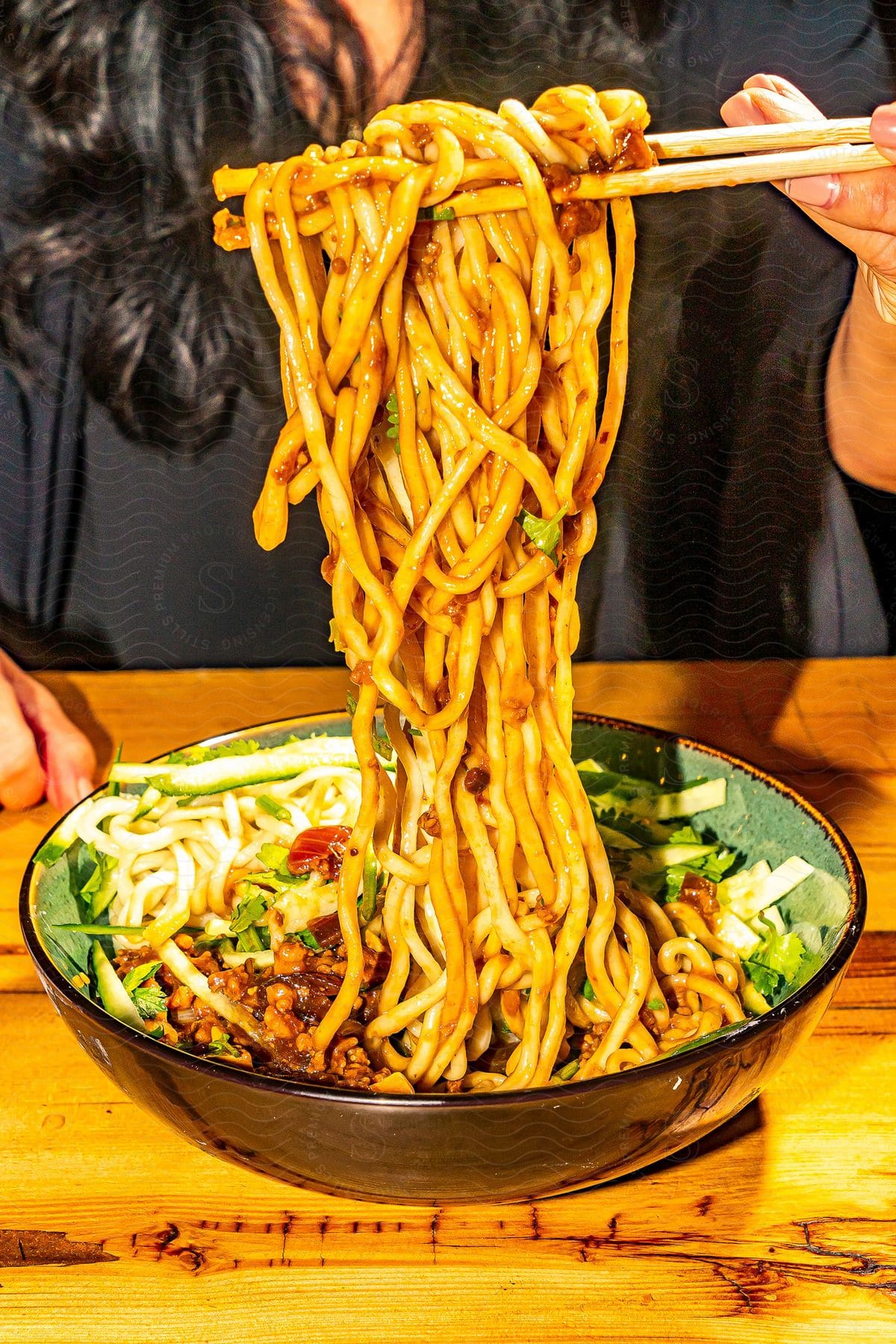 A woman picking up asian noodles with chopsticks