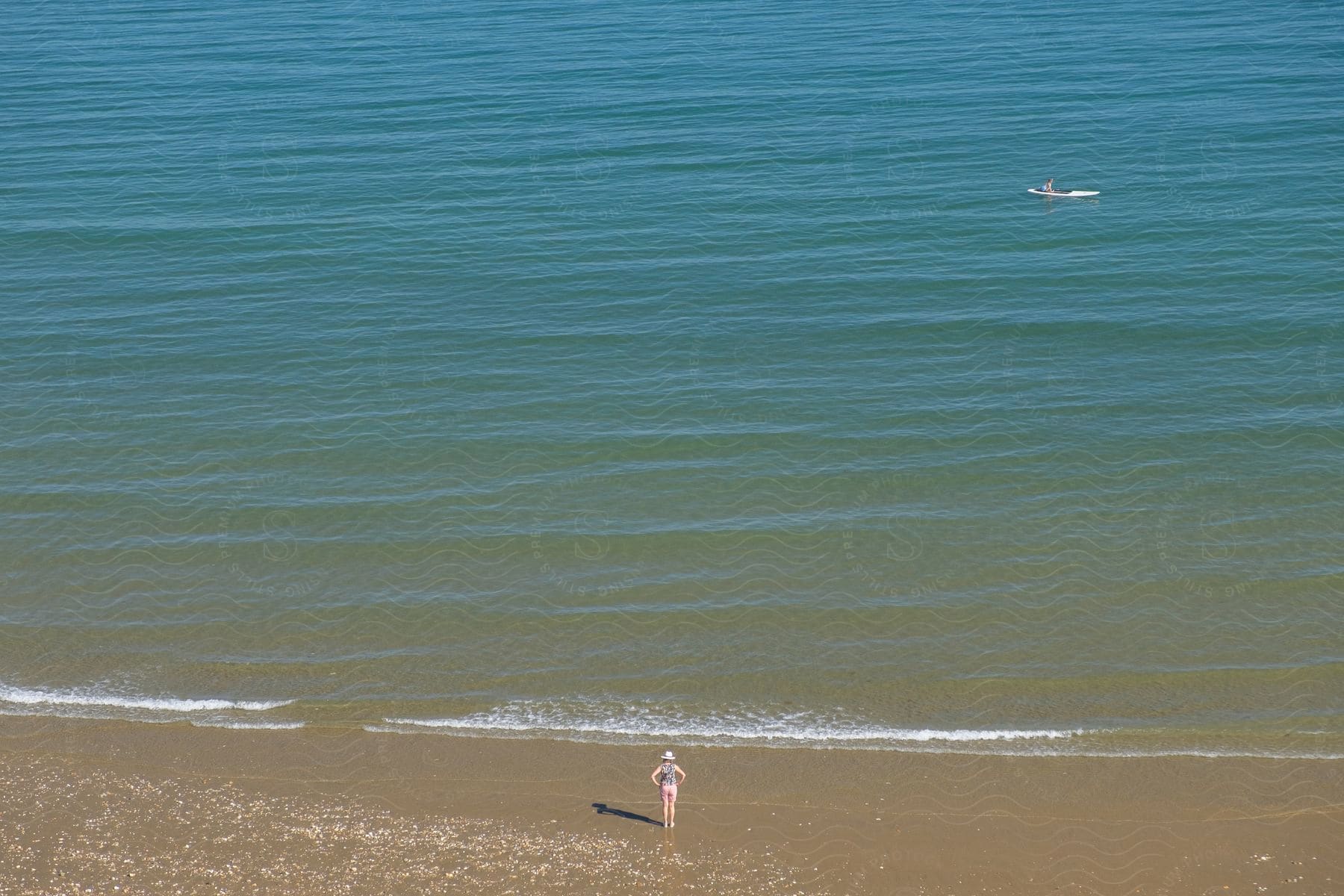 A woman stands at the coastline of a sandy beach