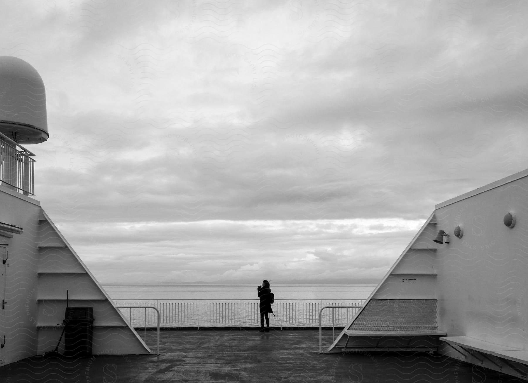 A woman takes pictures on the edge of a ship deck on a cloudy day