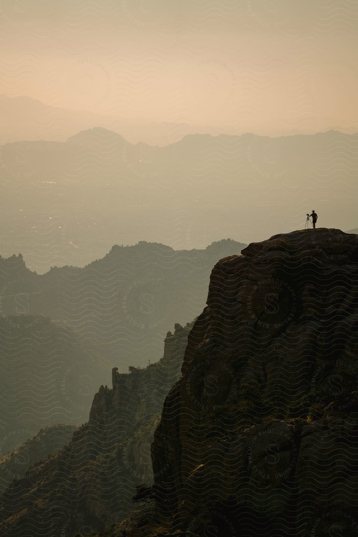 A person captures the view of a hazy valley and distant mountains from the top of a mountain with a tripod