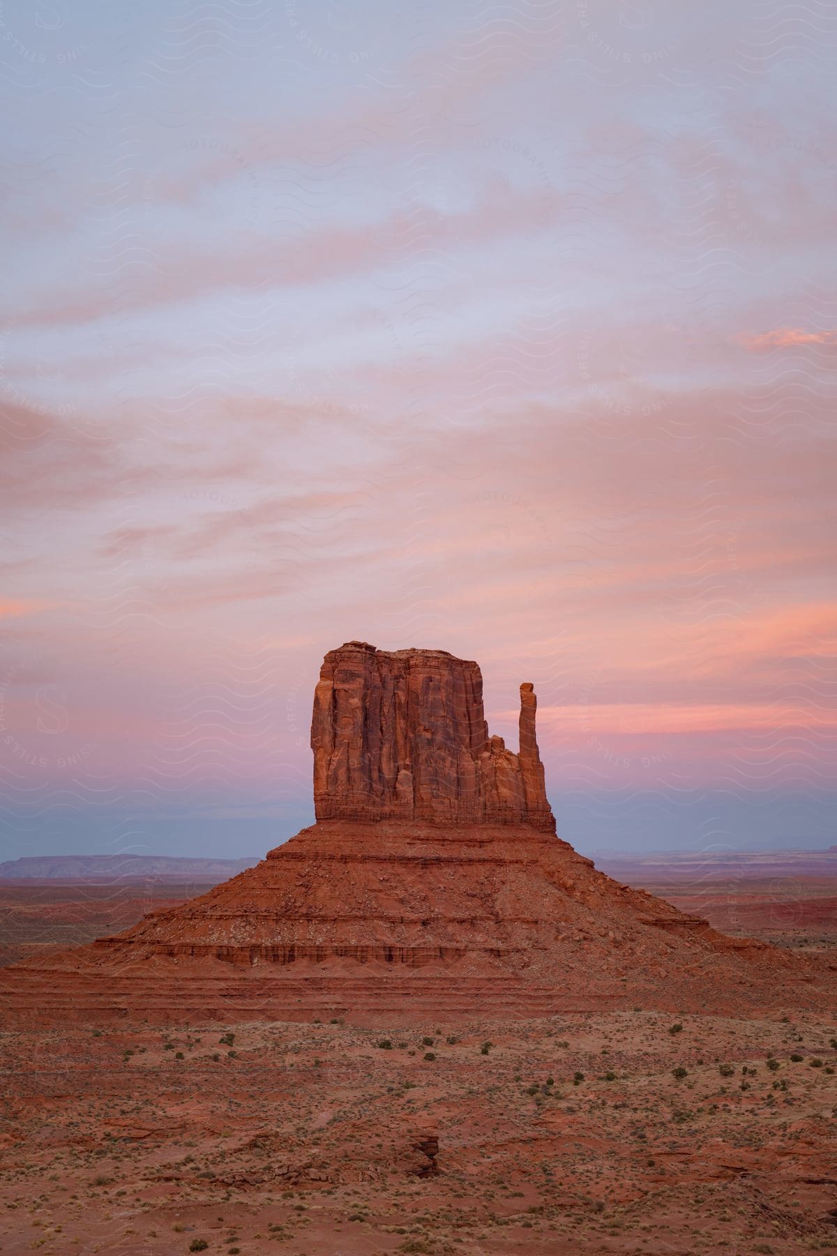 A tall rock formation in a desert mesa plateau under a pink and purple sky