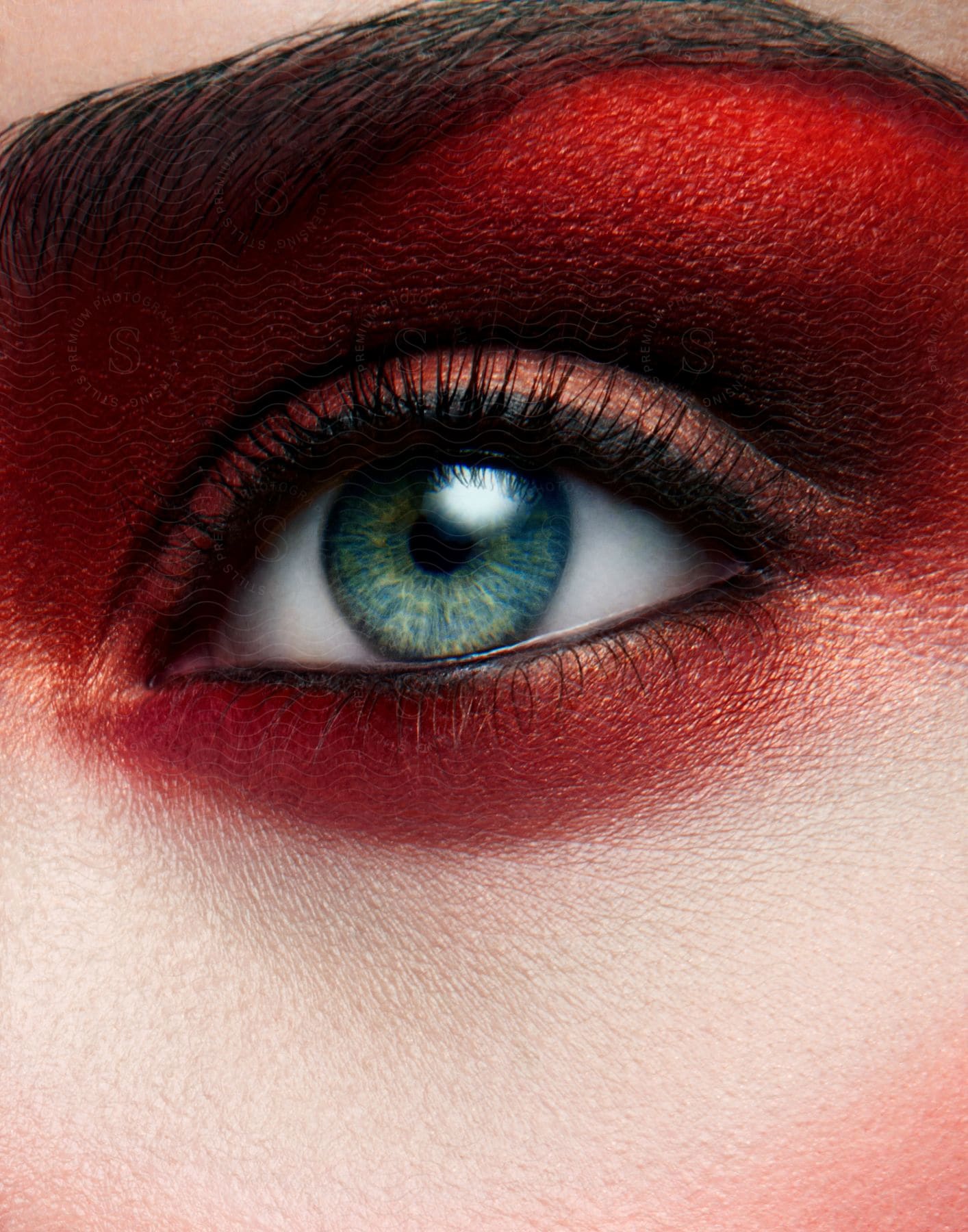 A womans blue eye with red eyeshadow around it