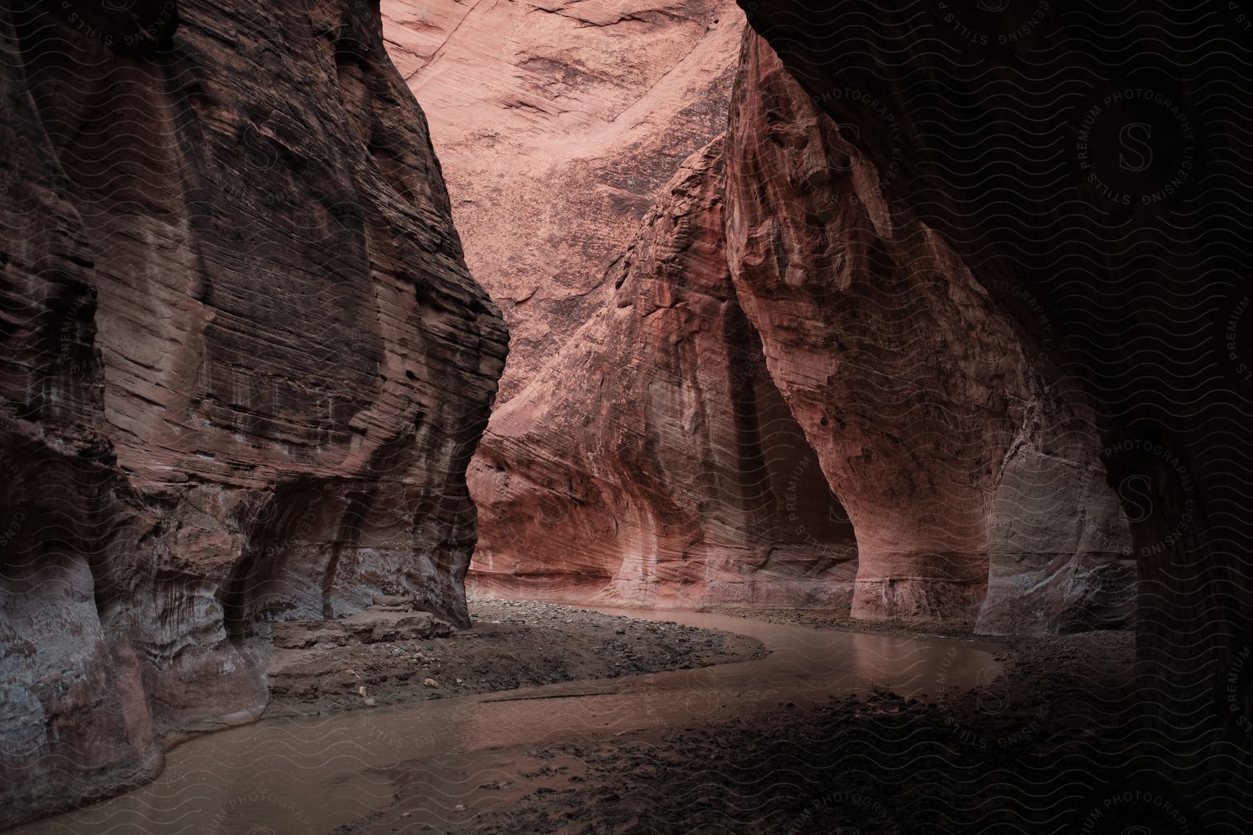 A stream flows between mountain canyons and past a cave in the side of a cliff