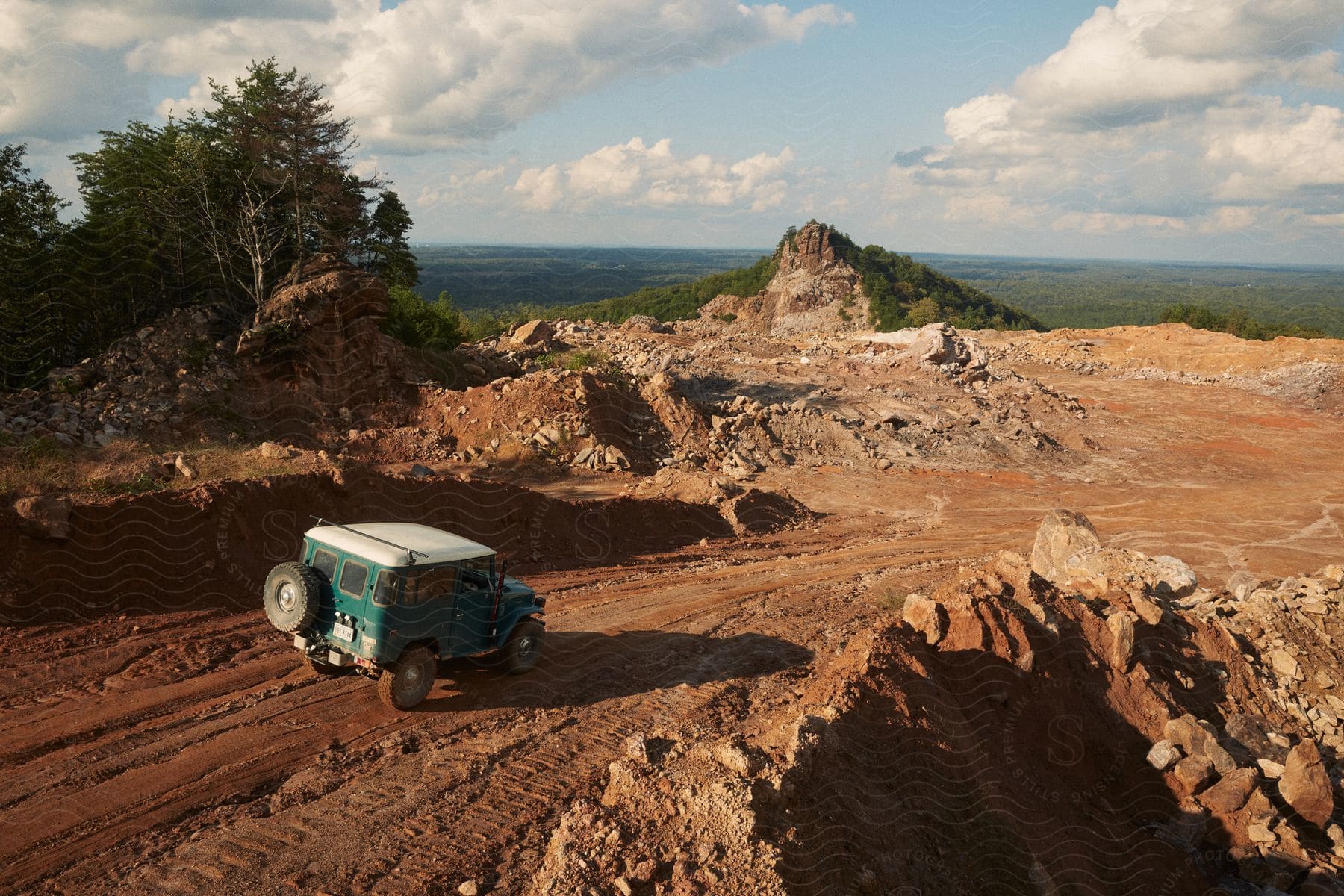 A jeep drives down a dirt road on a hilltop surrounded by a forest