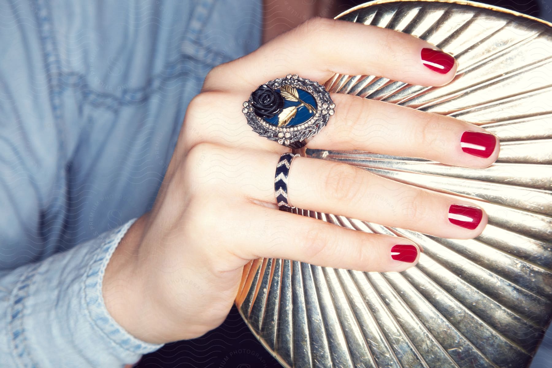 A womans hand with painted nails and ornate ring holding a metal purse