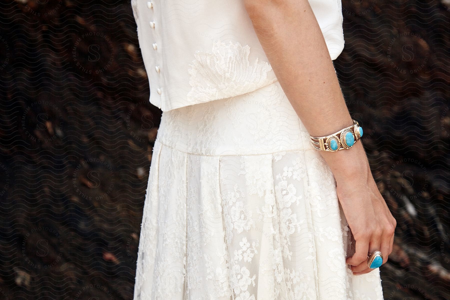 A woman wearing a white lace dress with a blue oval ring and gold bracelet