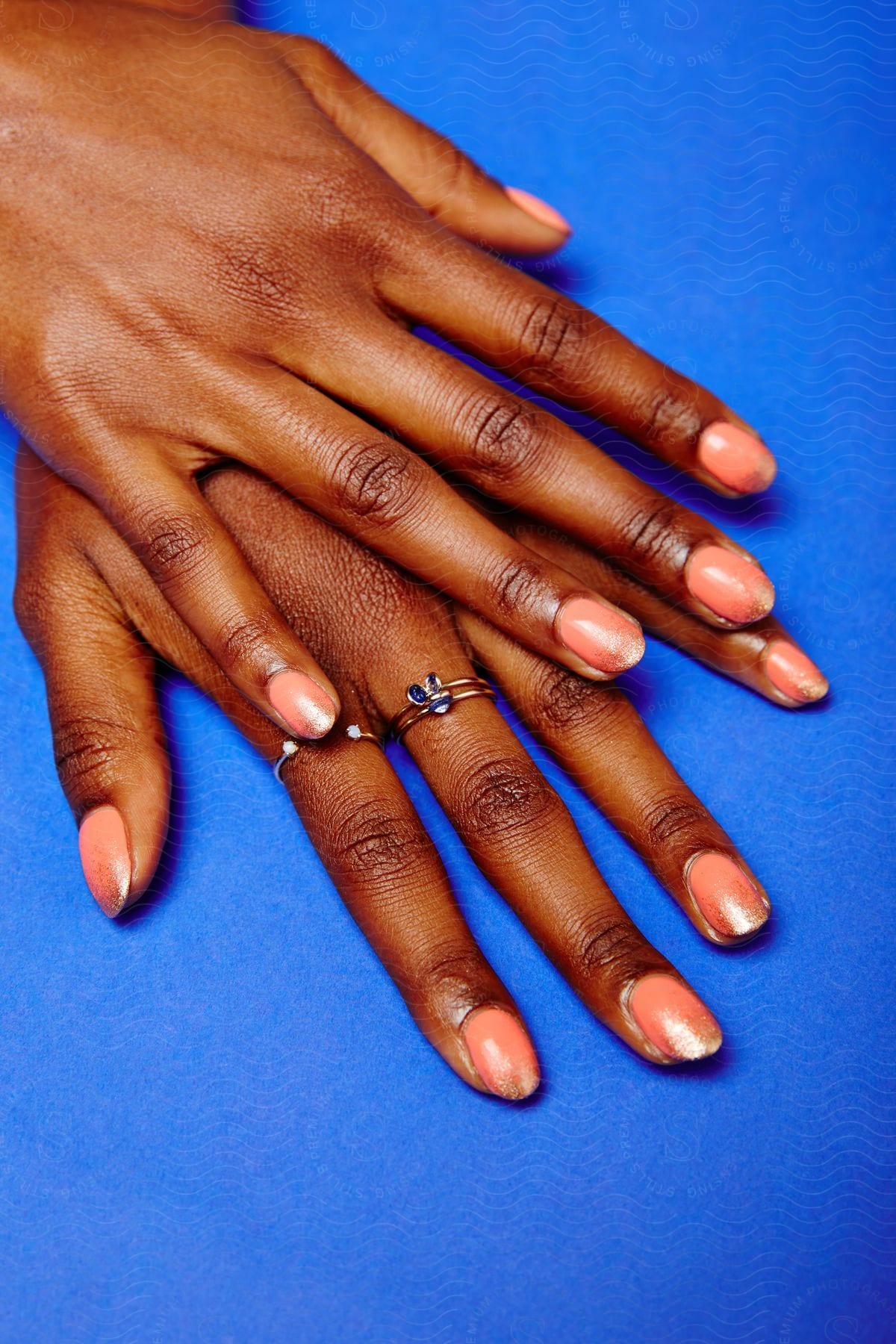 A black womans hands posing with rings over a blue surface