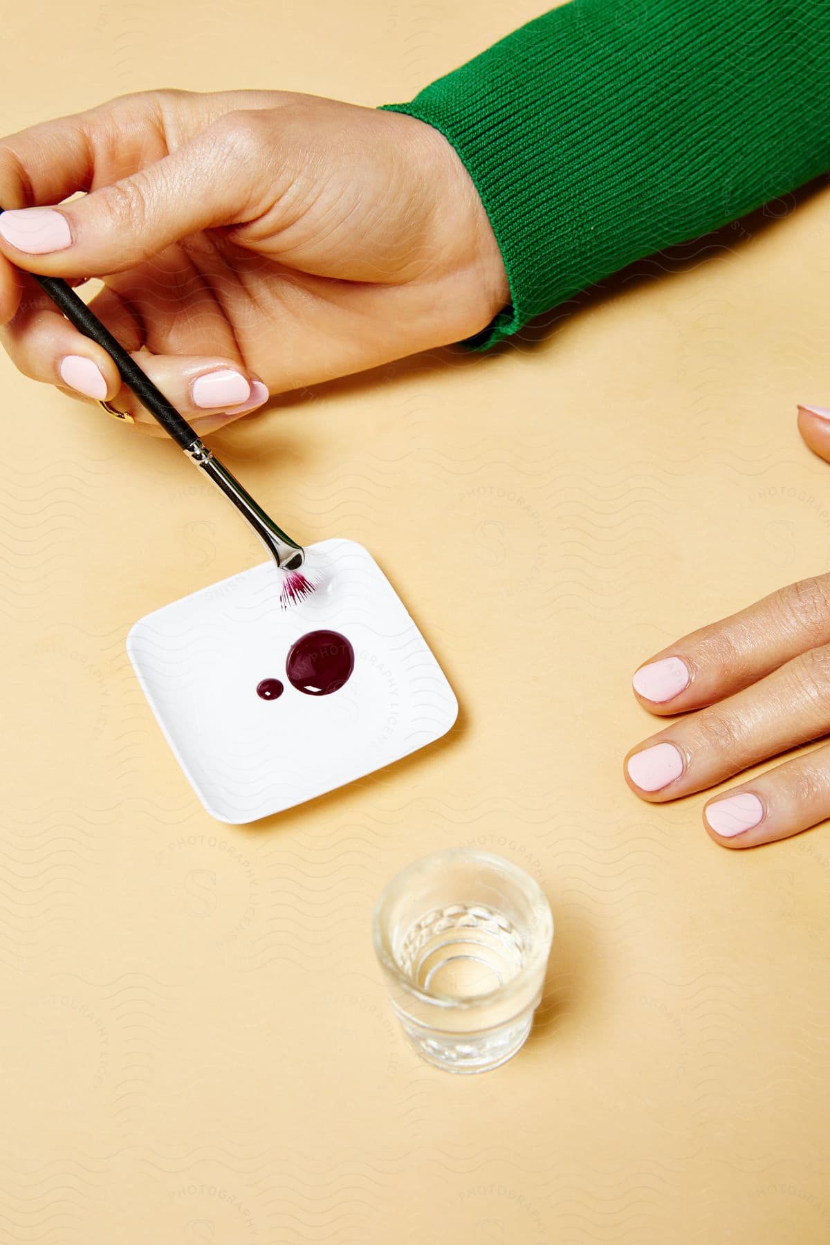 A woman using a paint brush with red paint on a small plate