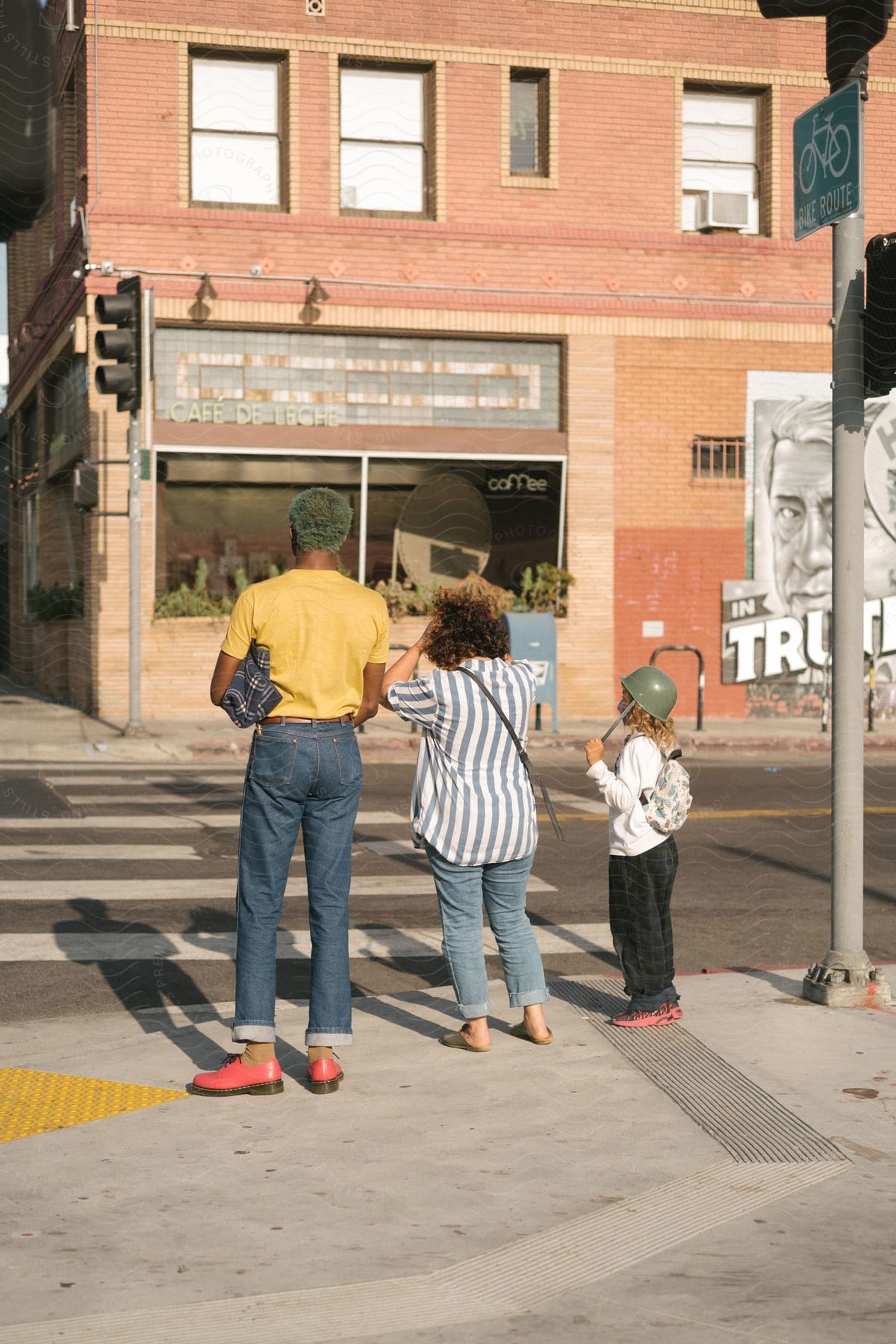 A family of three waits to cross the street towards a brick building