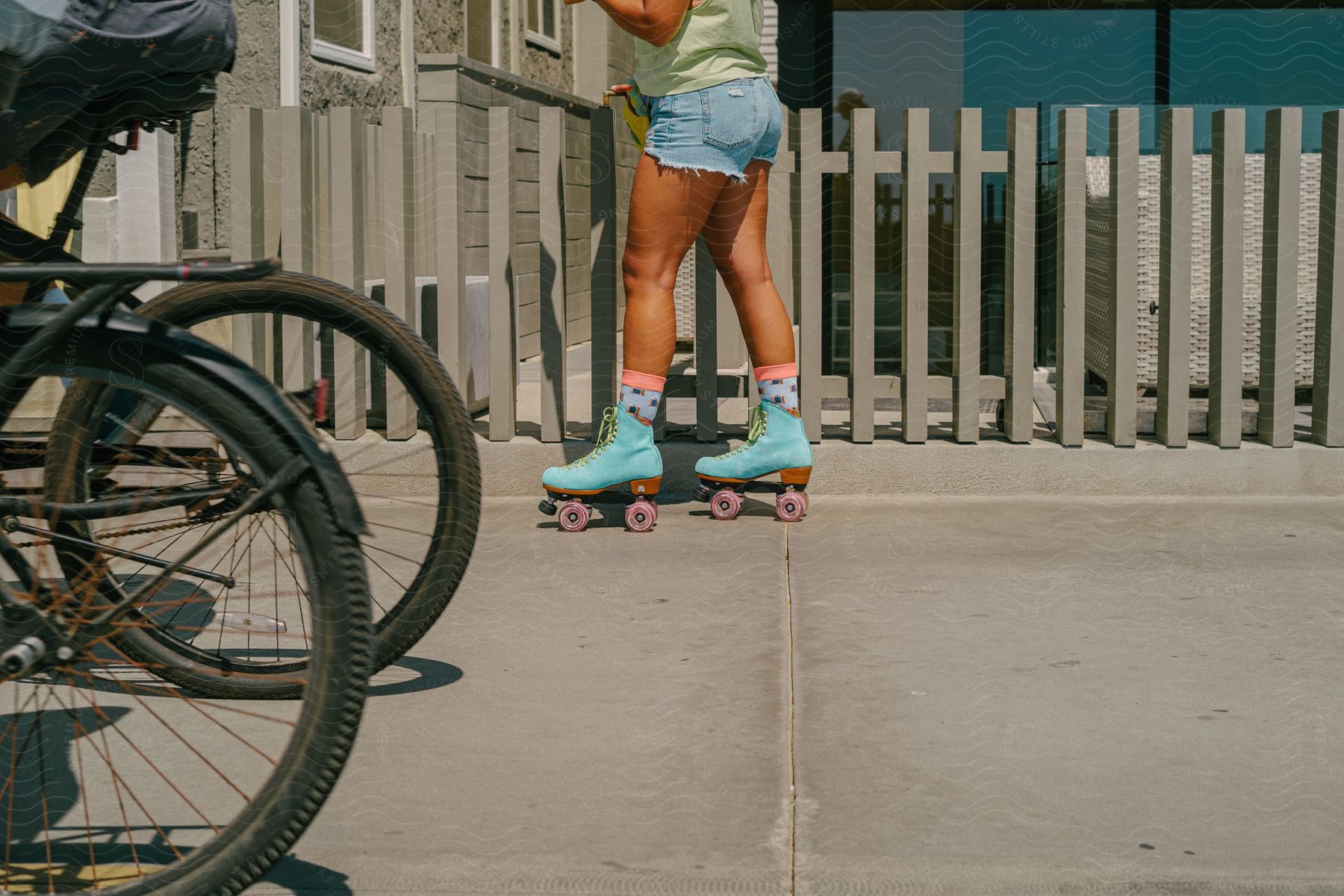 A woman wearing shorts and roller skates stands next to a fence on the street