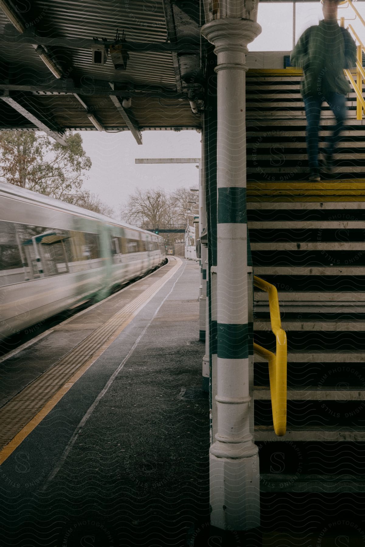 A person stands in a neutral subway station with architecture buildings and a train in the background