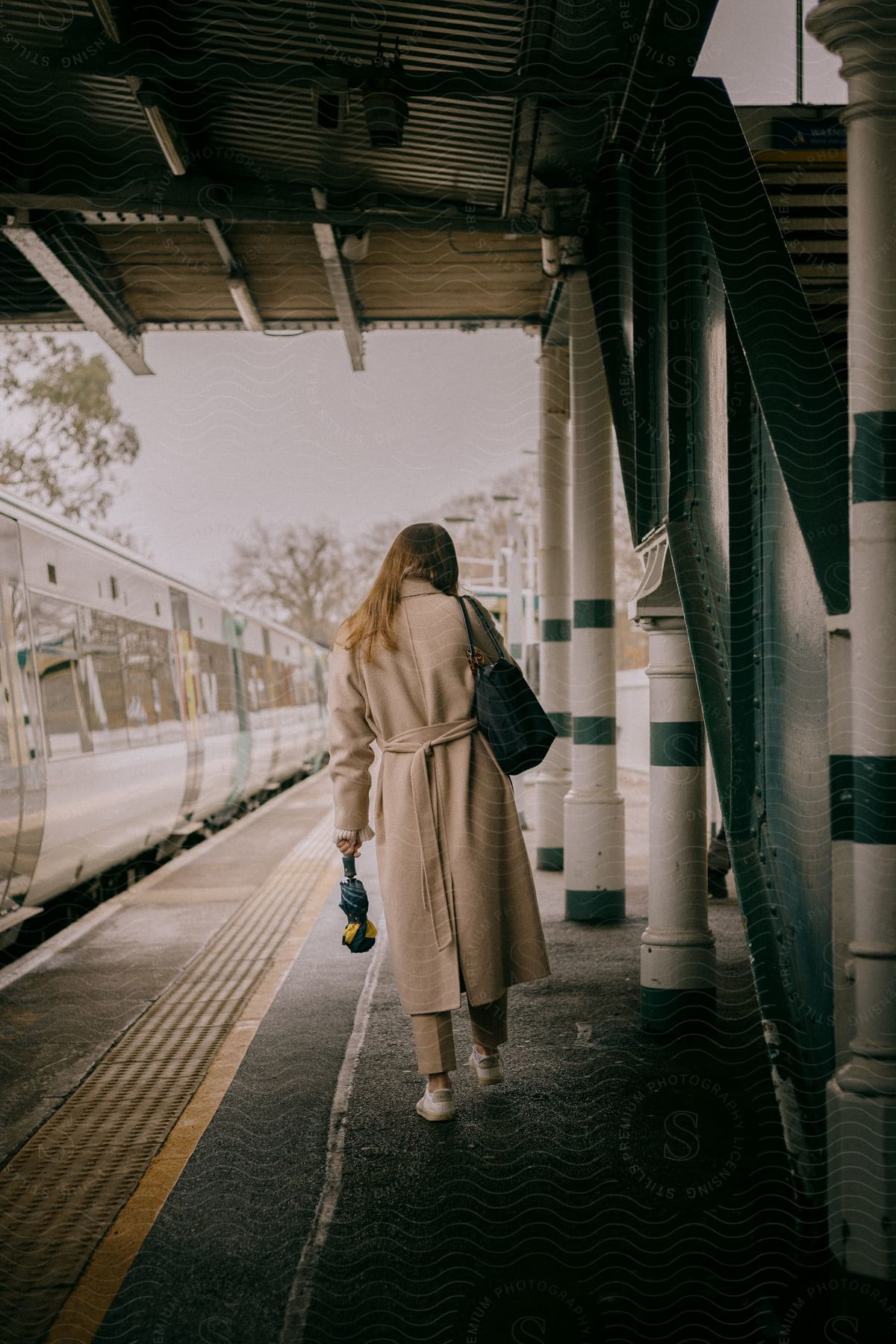 A woman walks next to a train at a train station wearing a coat