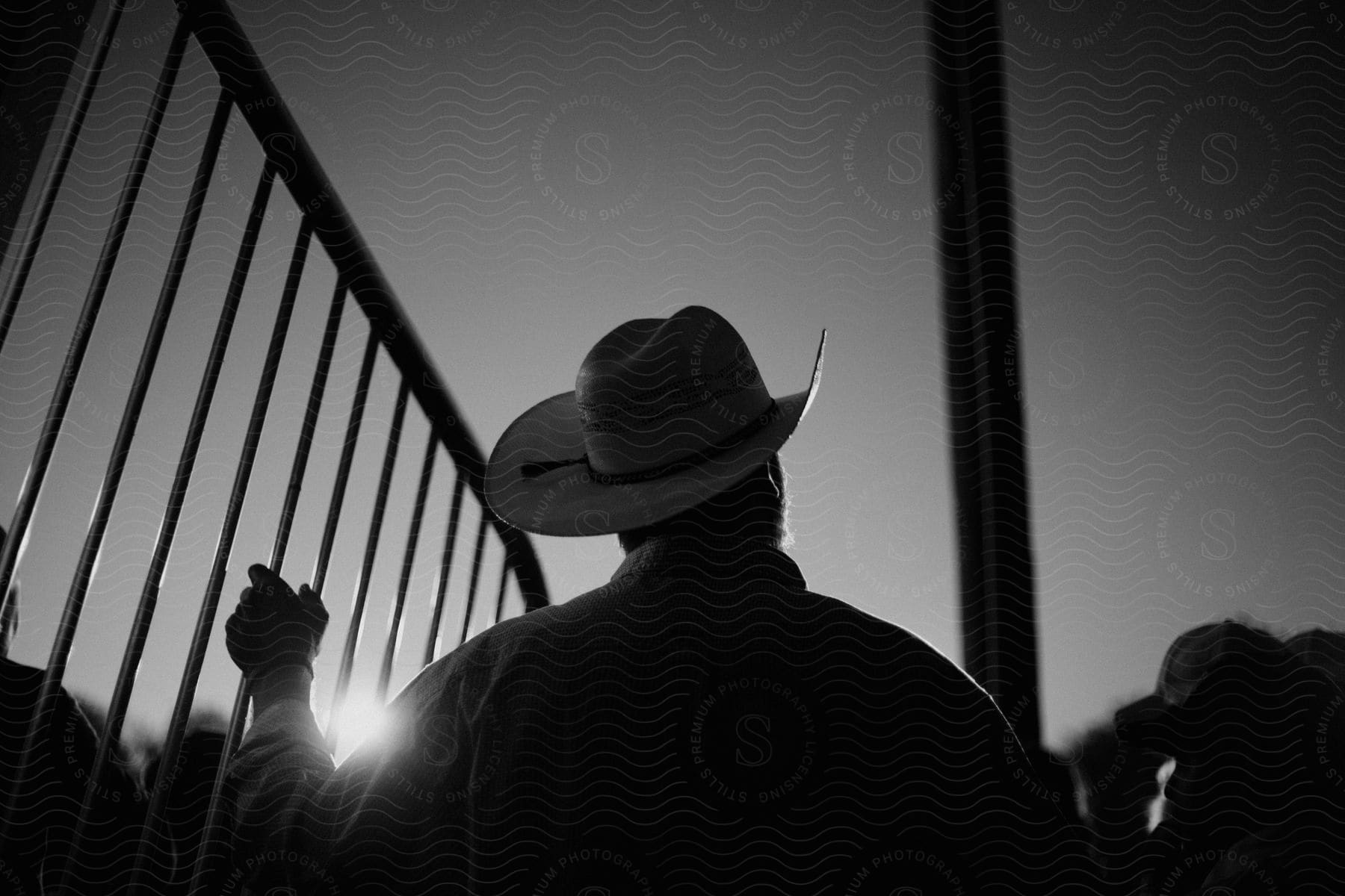 Stock photo of a person wearing a cowboy hat holds onto a fence outdoors at night