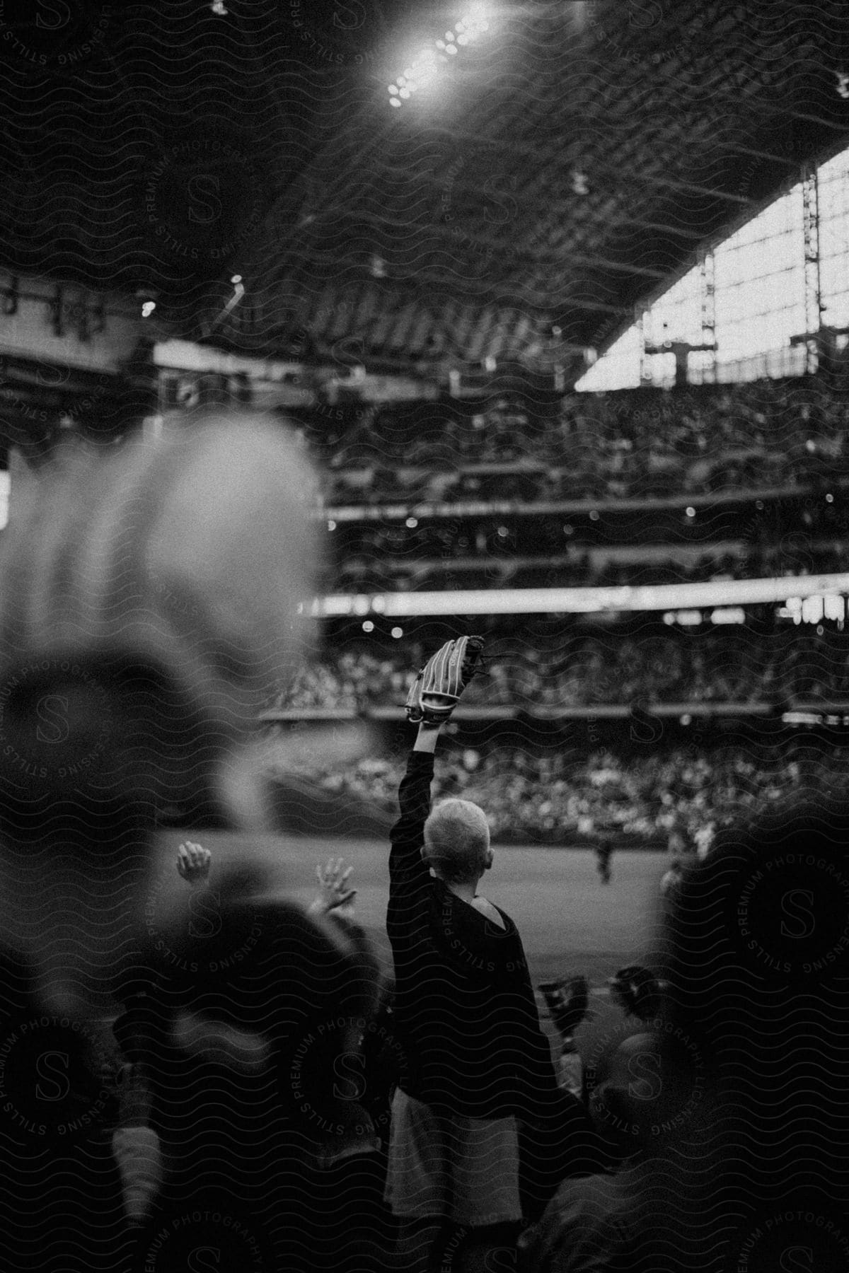 A young boy holds a baseball glove in a crowded baseball stadium