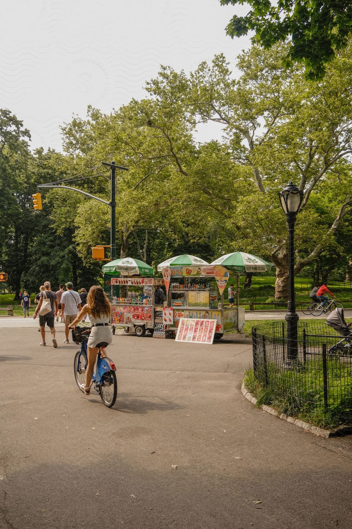 People enjoy a city park with bicycles and food carts near an intersection