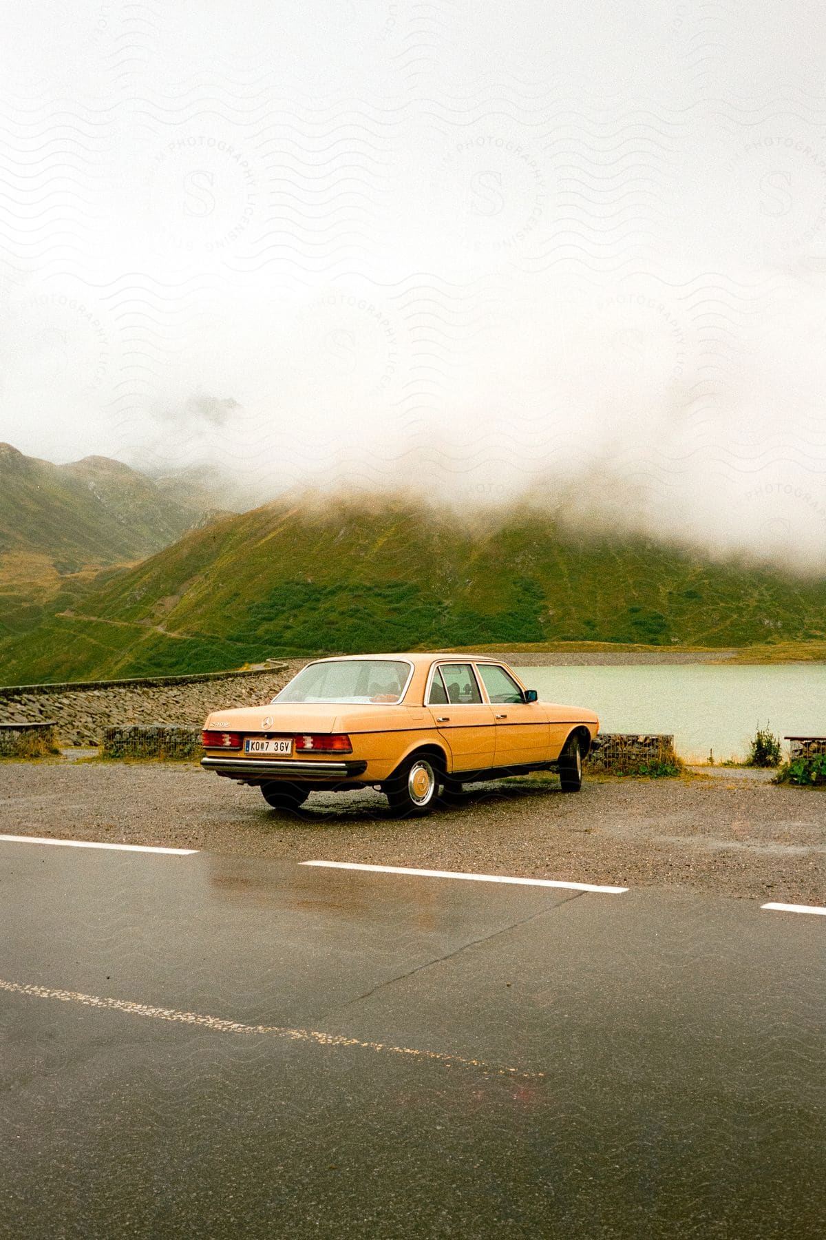 A yellow car parked on the shore across from misty mountains