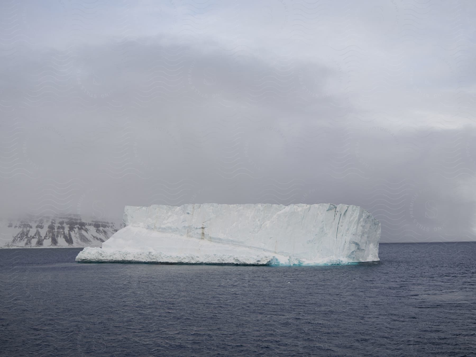 An ice berg in the ocean with fog and a snowcovered mountain in the distance