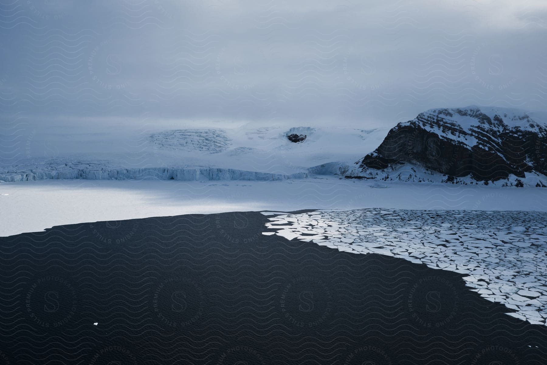 A frozen lake with floating ice and snowcovered mountains in the background