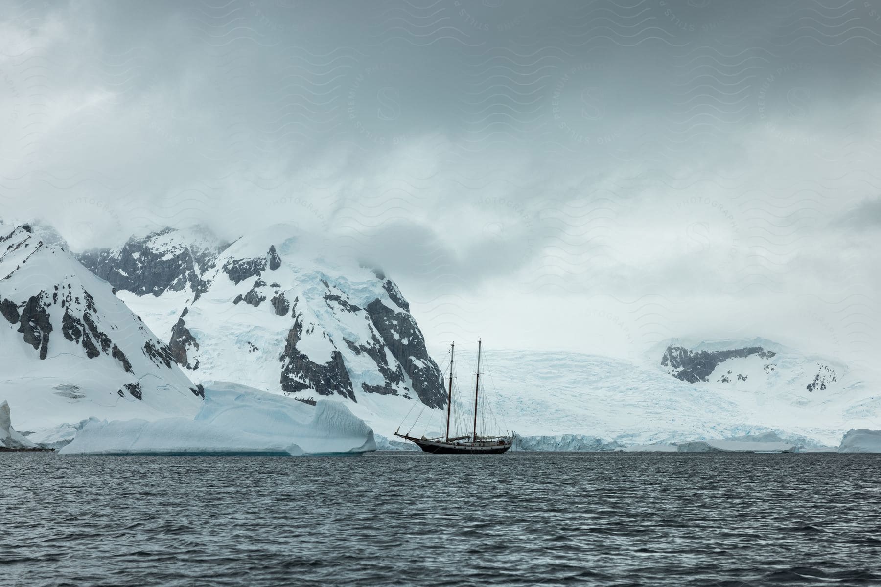 A sailboat is docked near a snowy bank in the ocean on a cloudy arctic day