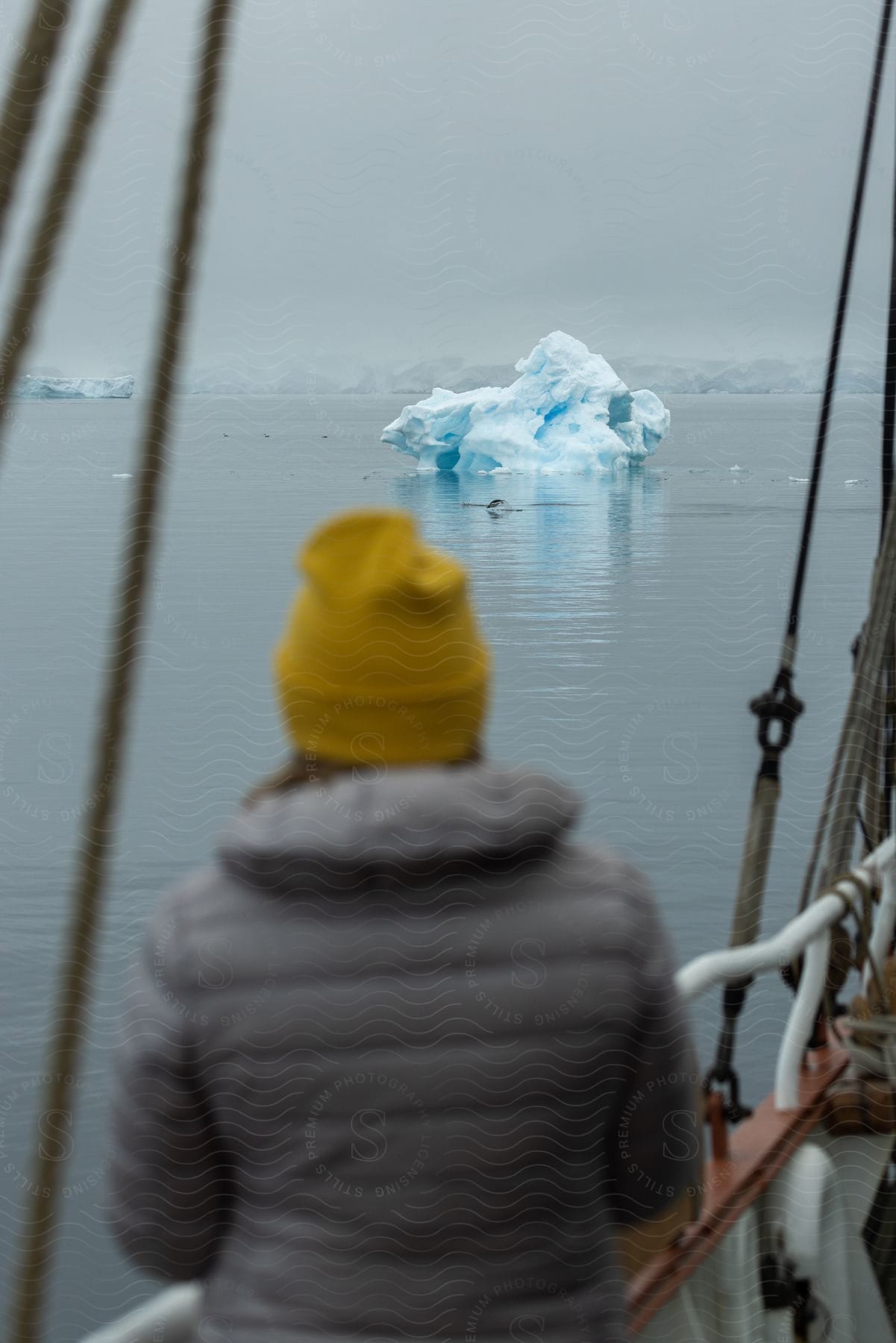 A woman wearing a yellow beanie is on a boat looking at the sea with a floating ice cap