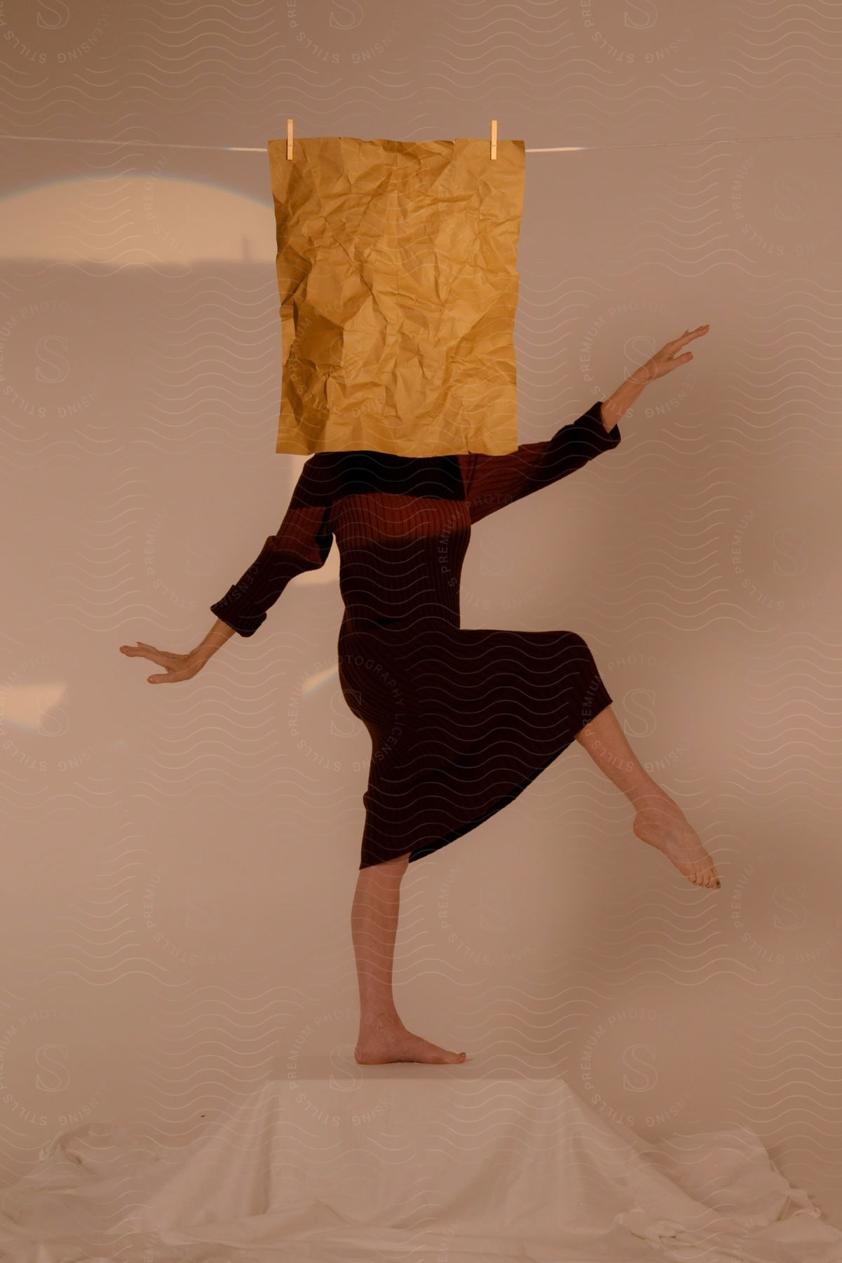 Stock photo of a woman dancer poses on a step wearing a ribbed sweater and long skirt with her face obscured by a crumbled piece of kraft paper pinned to a clothesline