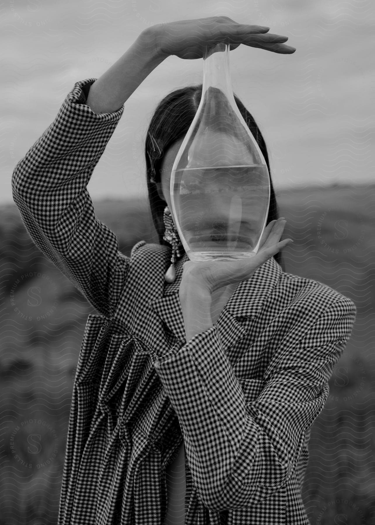 Stock photo of a woman holds a vase of water in front of her face in a field