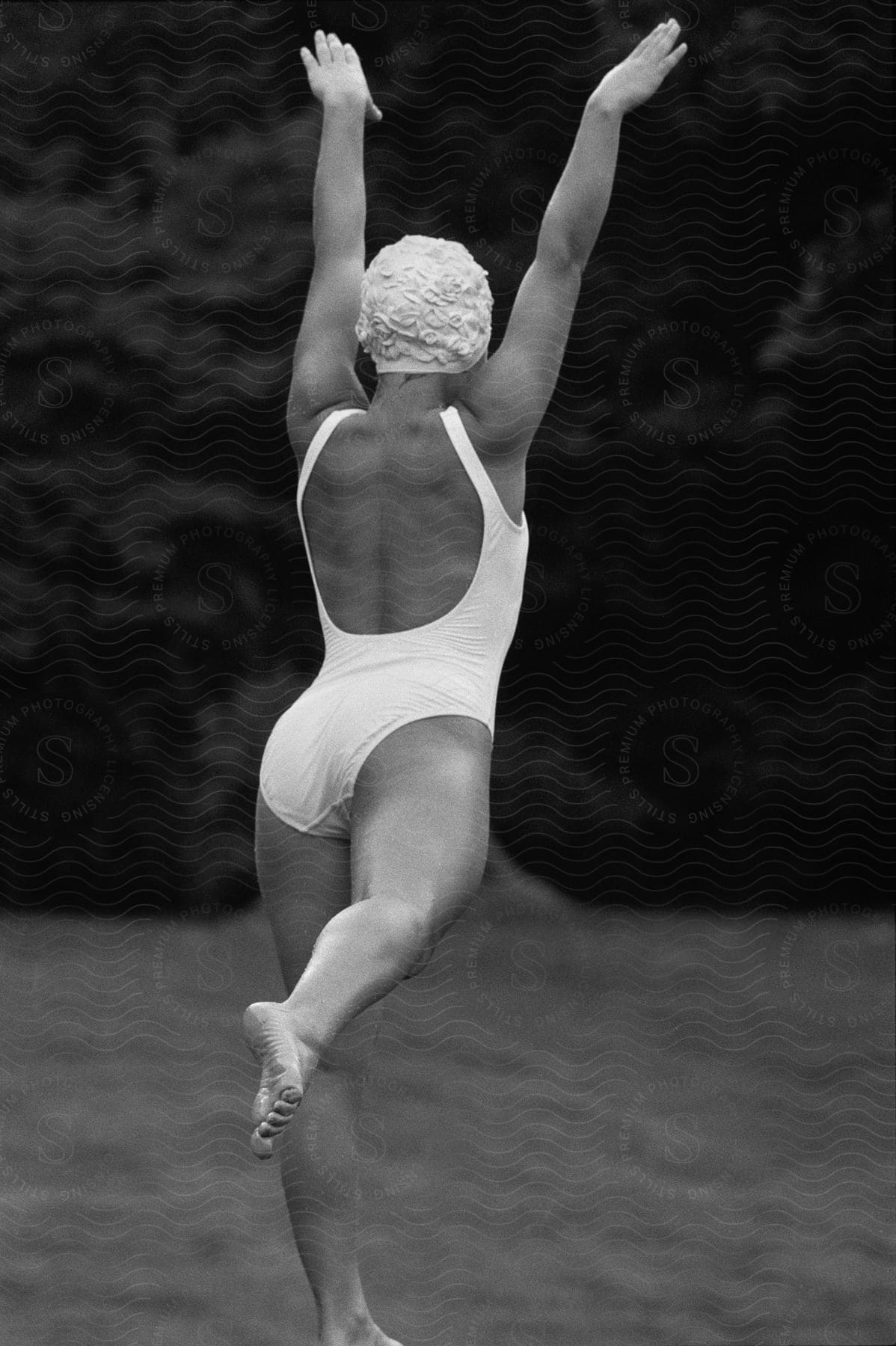 A woman wearing a bathing cap stands on a beach with her arms raised