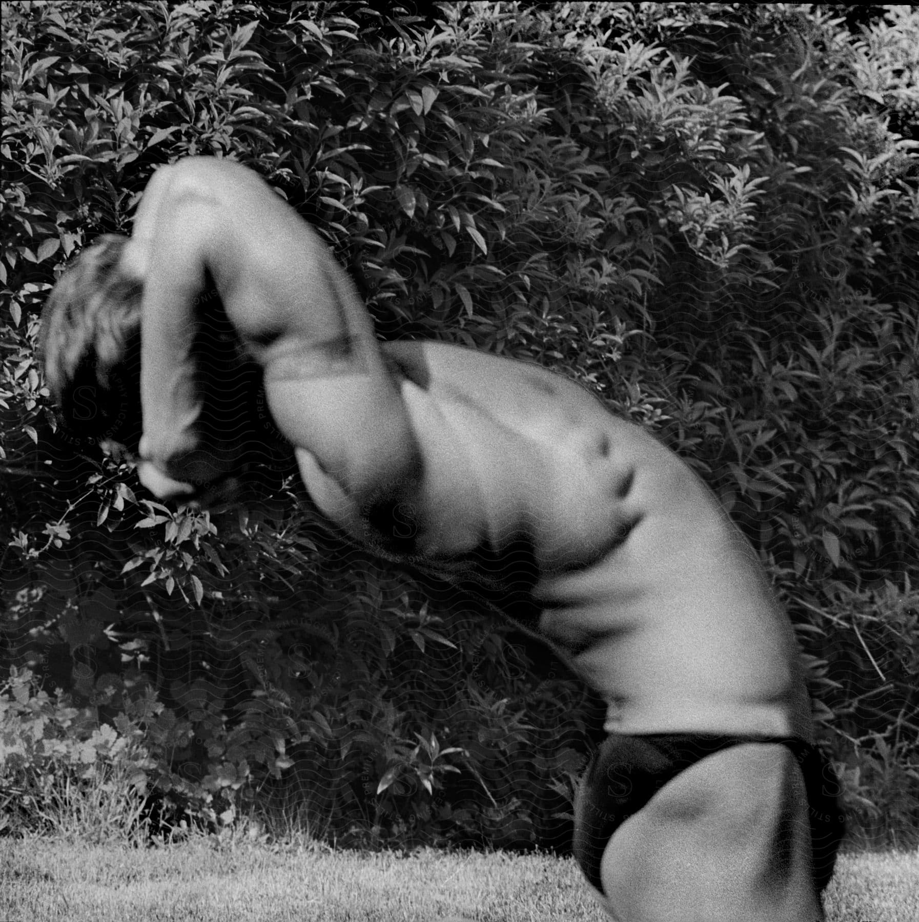 Stock photo of a man stretches his back in a black and white photo in front of a bush