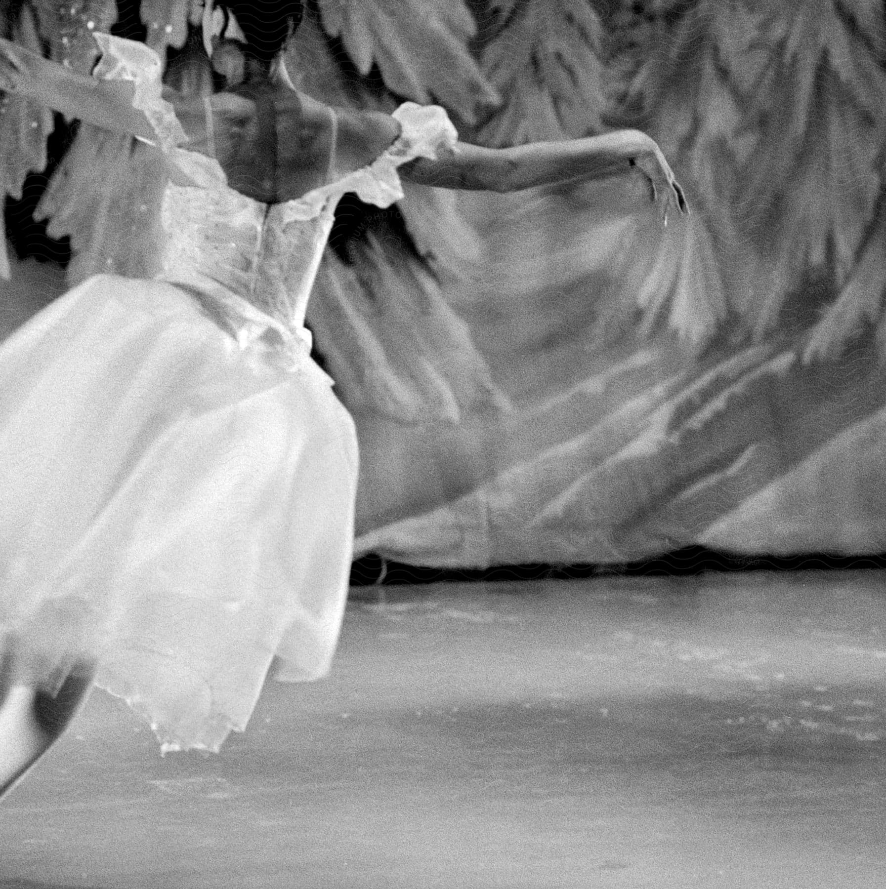 A ballerina wearing a white dress is seen dancing on a stage in black and white