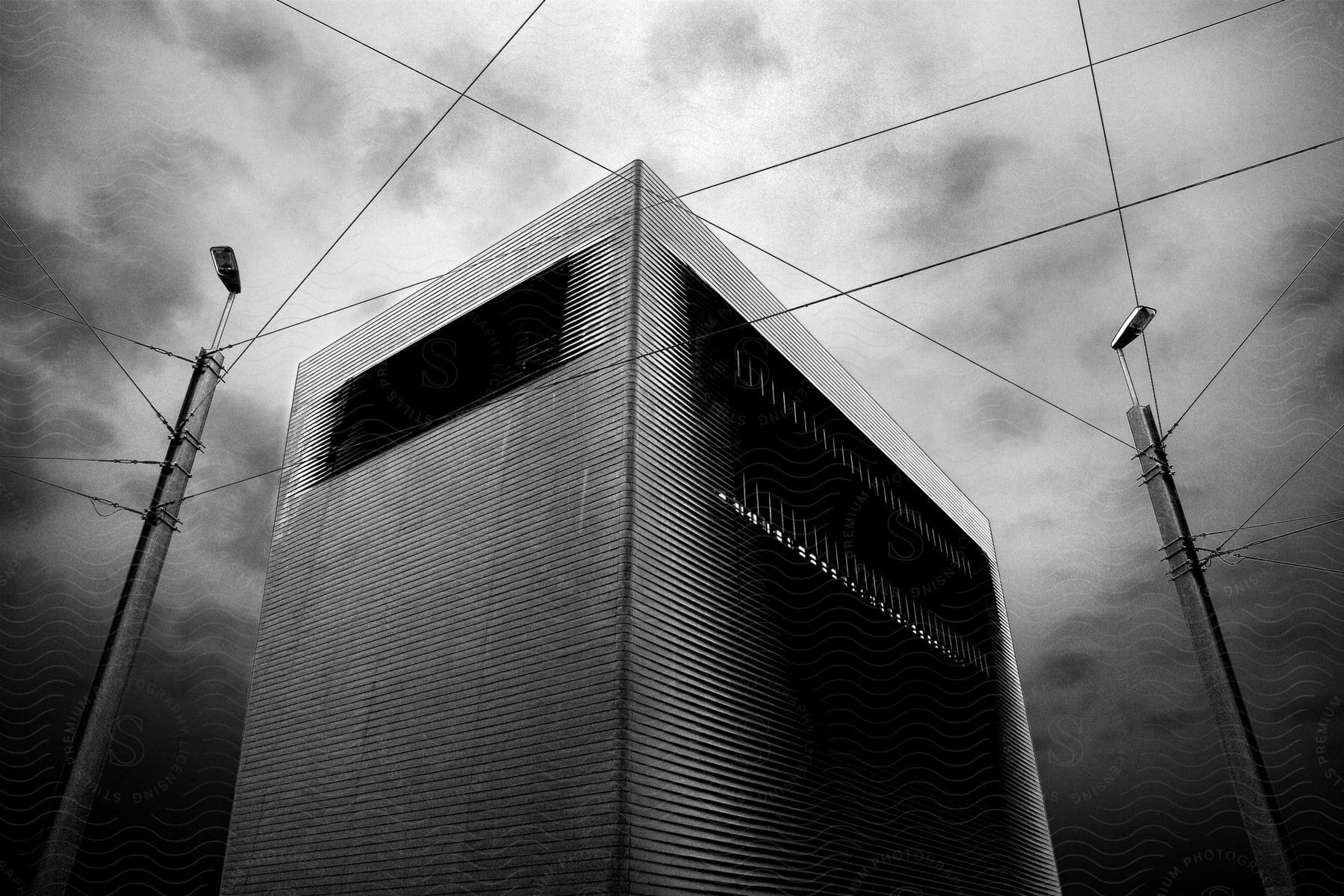 A tall windowless blackandwhite building with power lines against a sky background